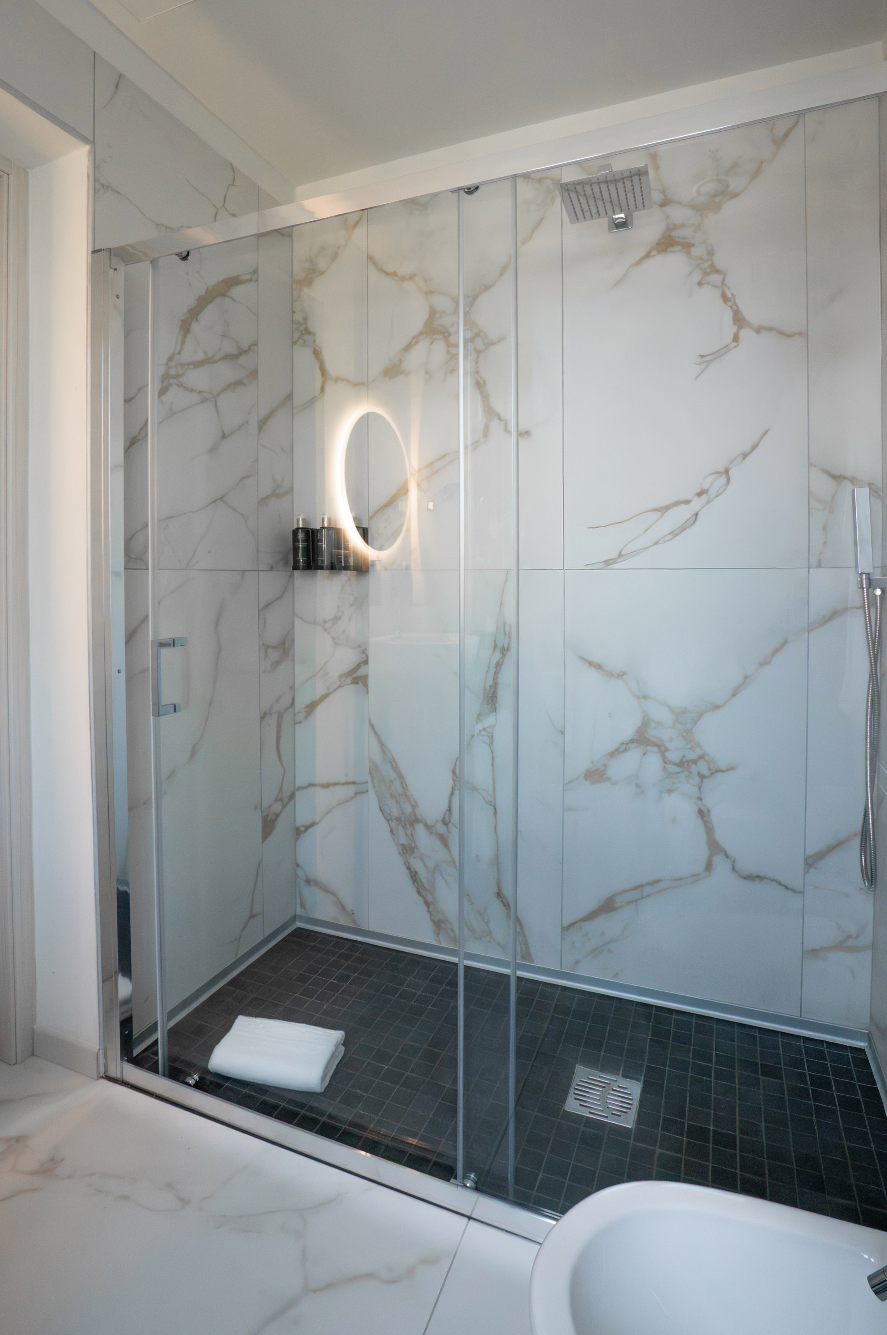 Modern bathroom shower with glass, white marble walls, and dark tiled floor.
