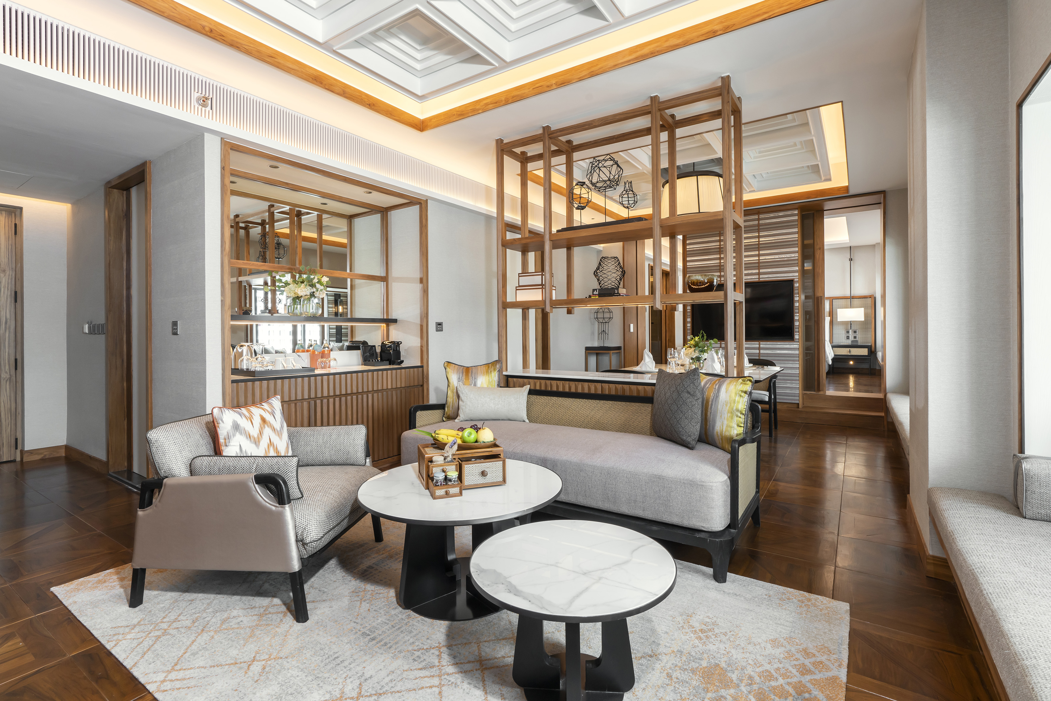 Luxury hotel suite living room with gray sofa, modern wooden shelves, marble tables.