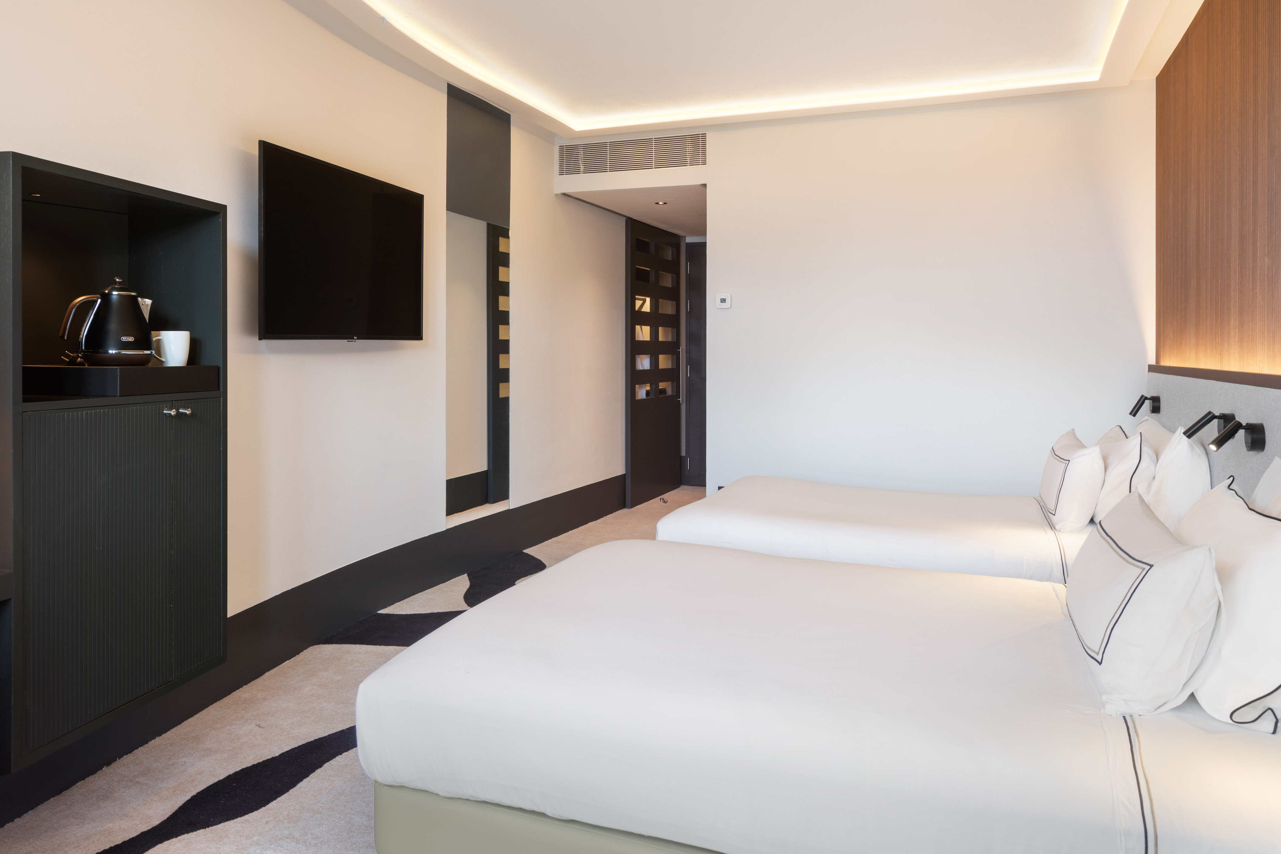 Contemporary hotel room featuring twin beds, smart TV, and coffee setup.