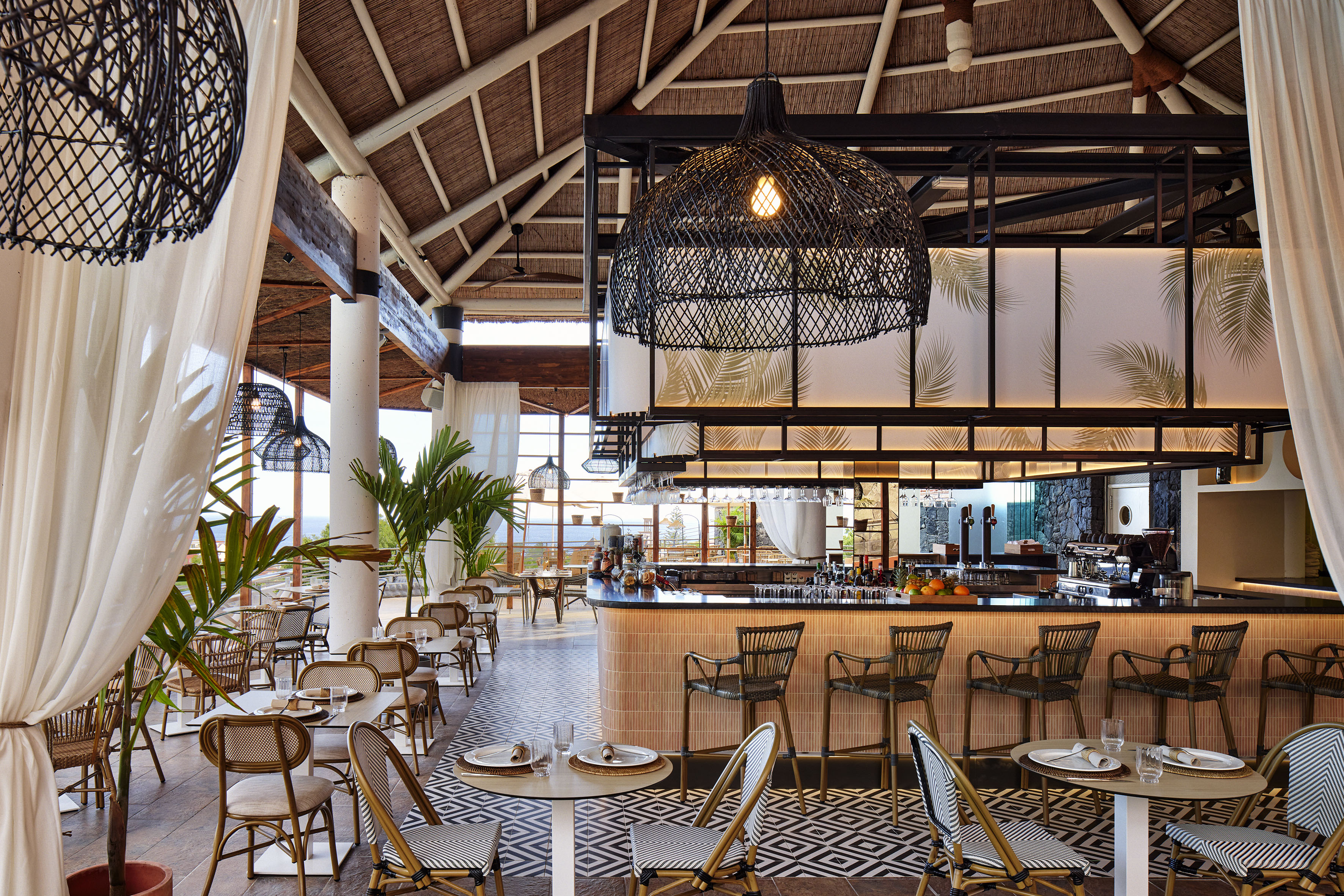 Tropical resort restaurant bar with woven lights, thatched roof, and ocean view.