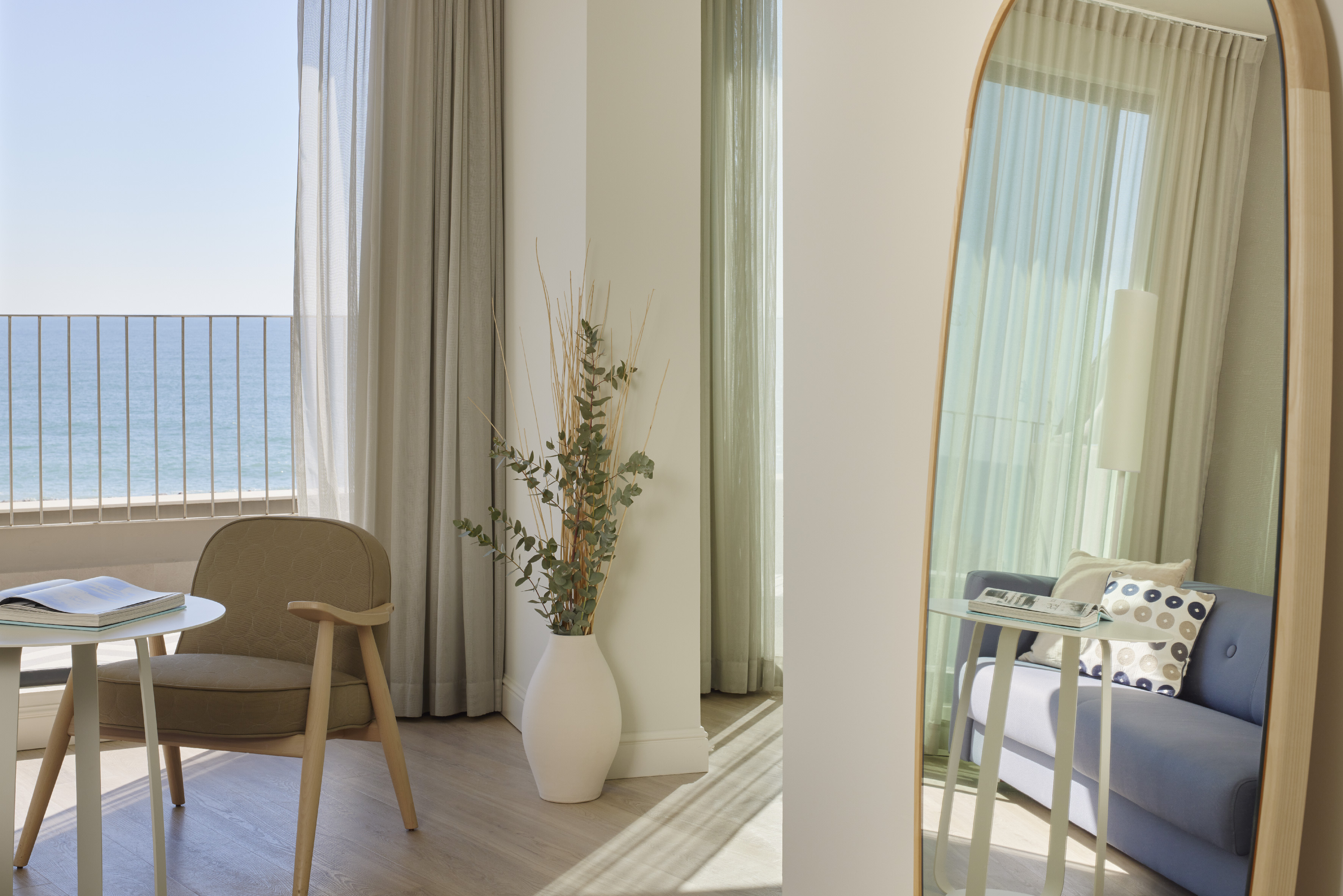 Coastal hotel room with ocean view, modern armchair, decorative vase, and mirror.