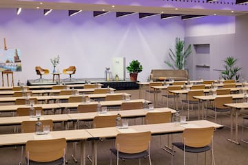 Modern conference room with rows of tables, chairs, stage, and contemporary decor.