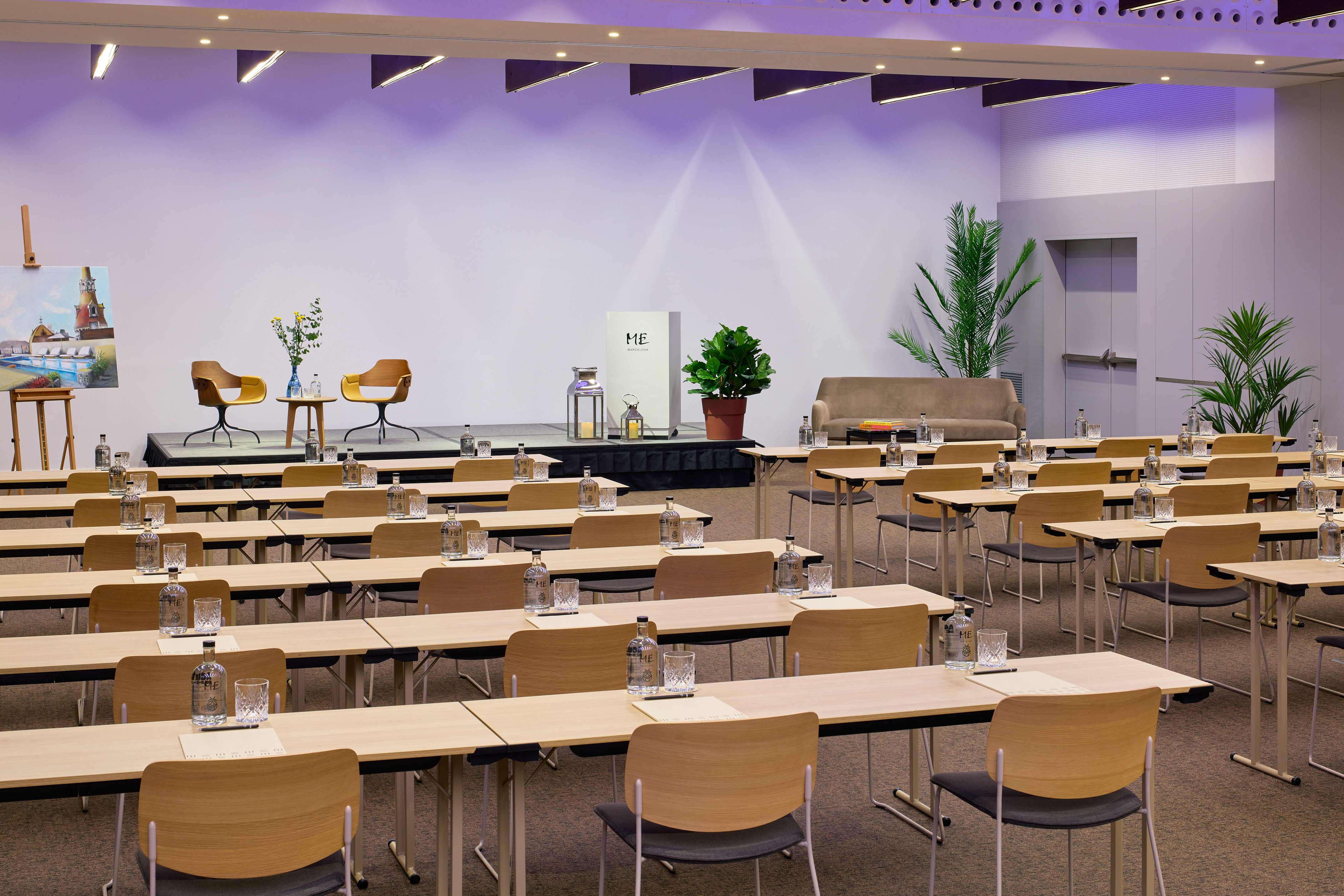 Empty hotel conference room with rows of tables, chairs, and stage.