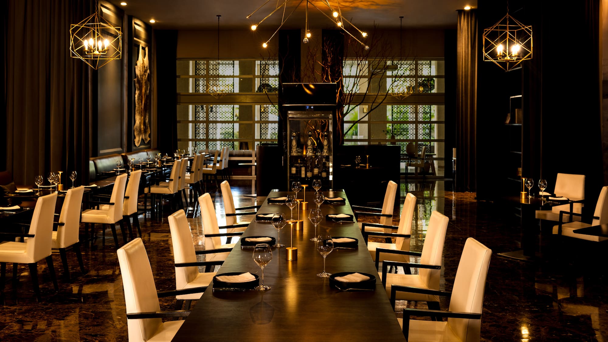 Modern luxury restaurant dining room, long table, cream chairs, chandeliers.