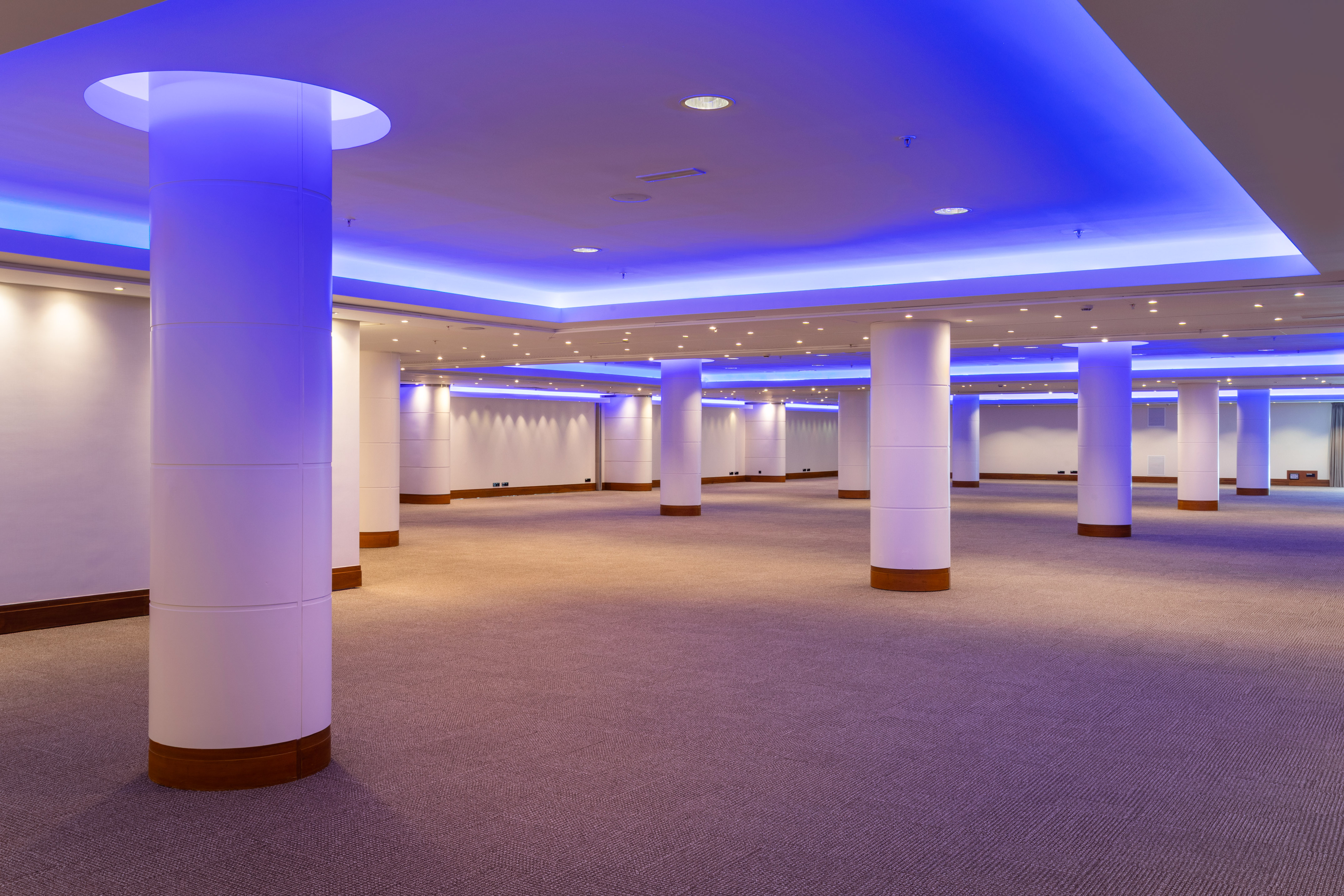 Empty event hall with blue ambient lighting and white support pillars.