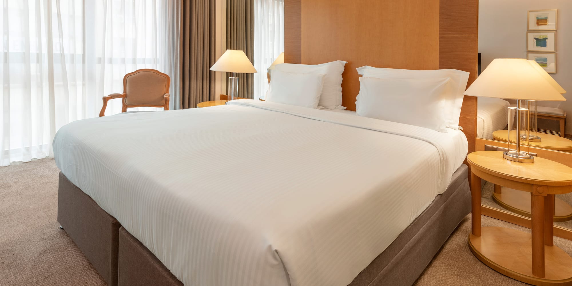 Modern hotel room with king bed, white sheets, wooden headboard, and bedside lamps.