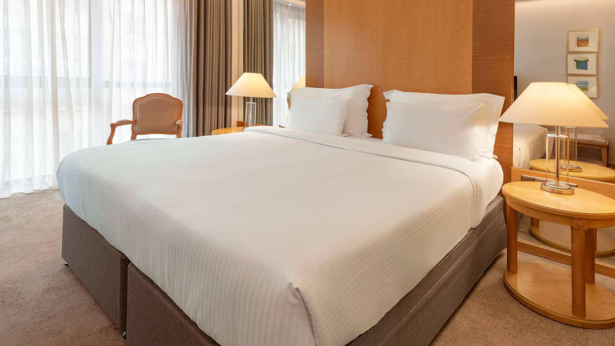 Modern hotel room with king bed, white sheets, wooden headboard, and bedside lamps.