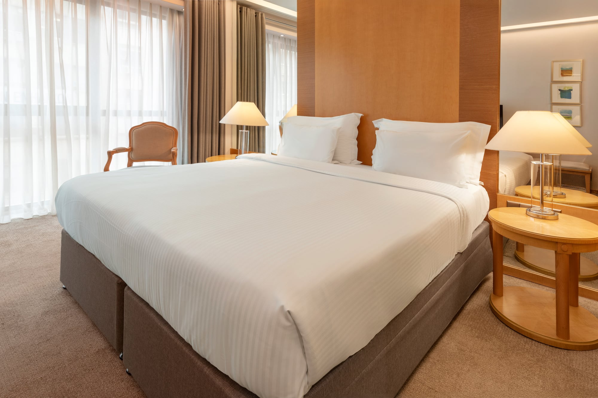 Modern hotel room with king bed, white sheets, wooden headboard, and bedside lamps.