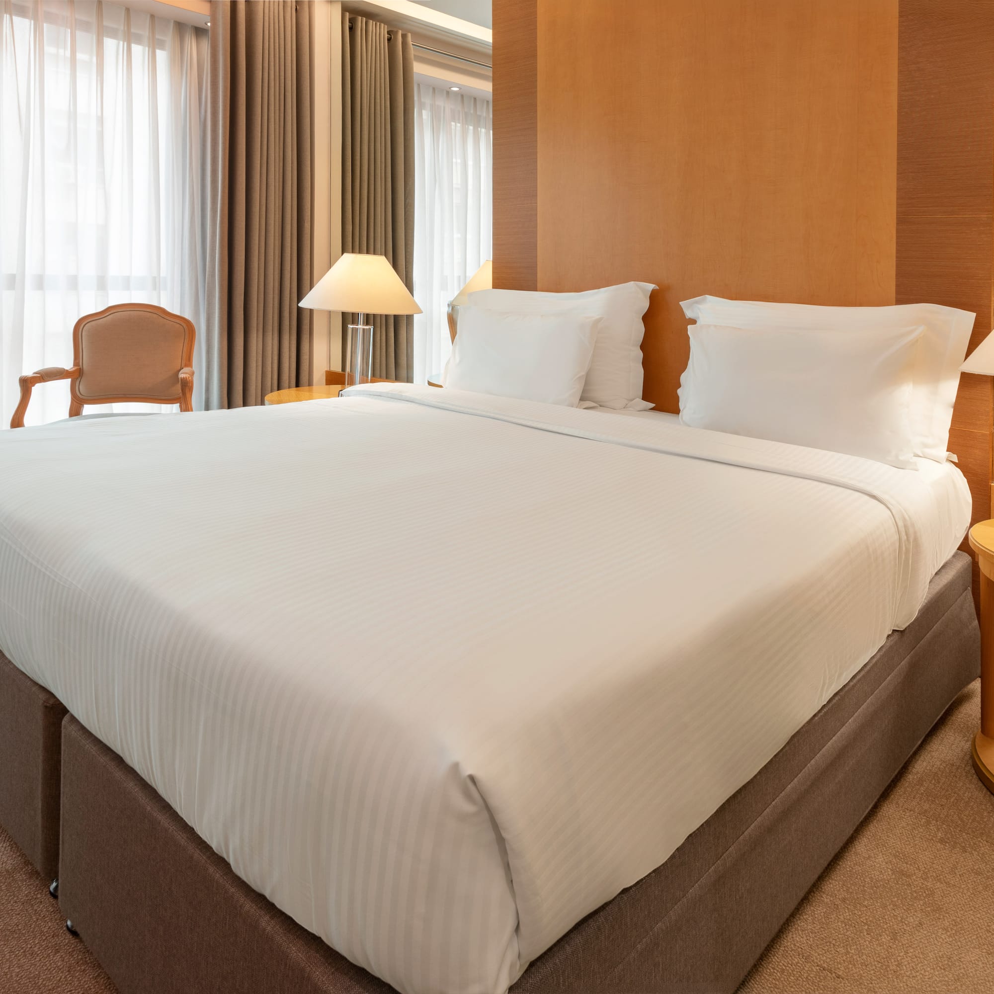 Modern hotel room with king bed, white sheets, wooden headboard, and bedside lamps.