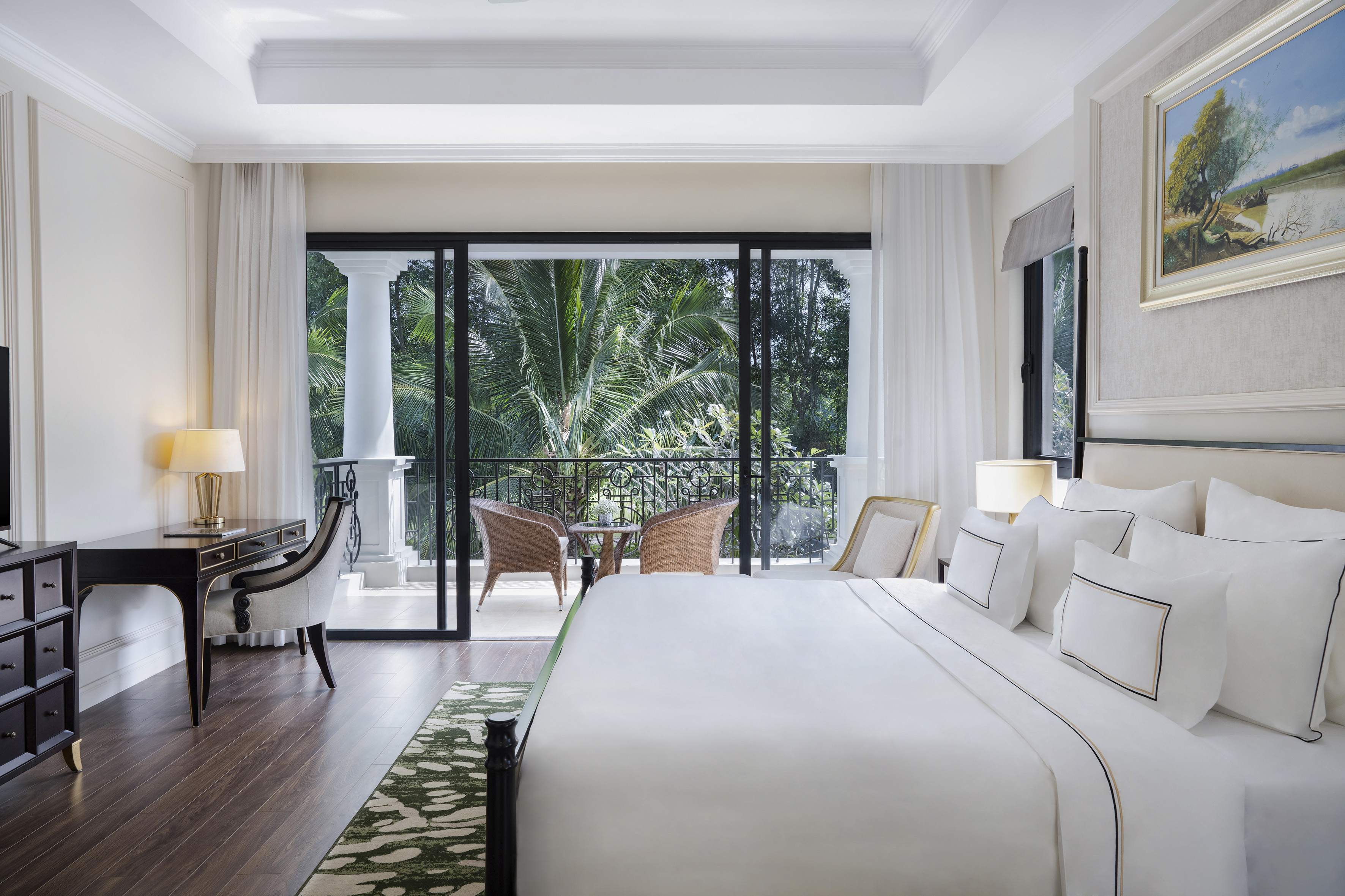 Elegant hotel suite with king bed, desk, and tropical balcony view.