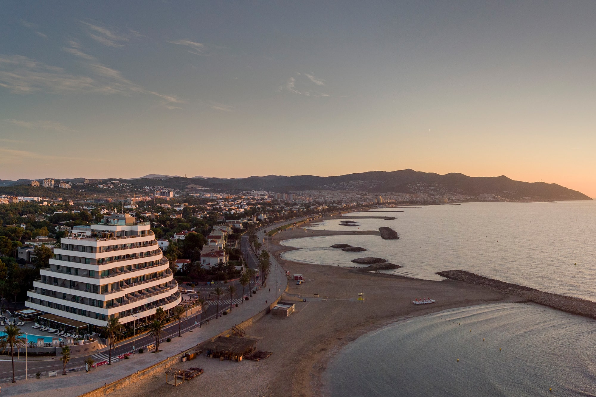 Aerial view: Modern coastal resort hotel, beach, and sunrise over ocean.
