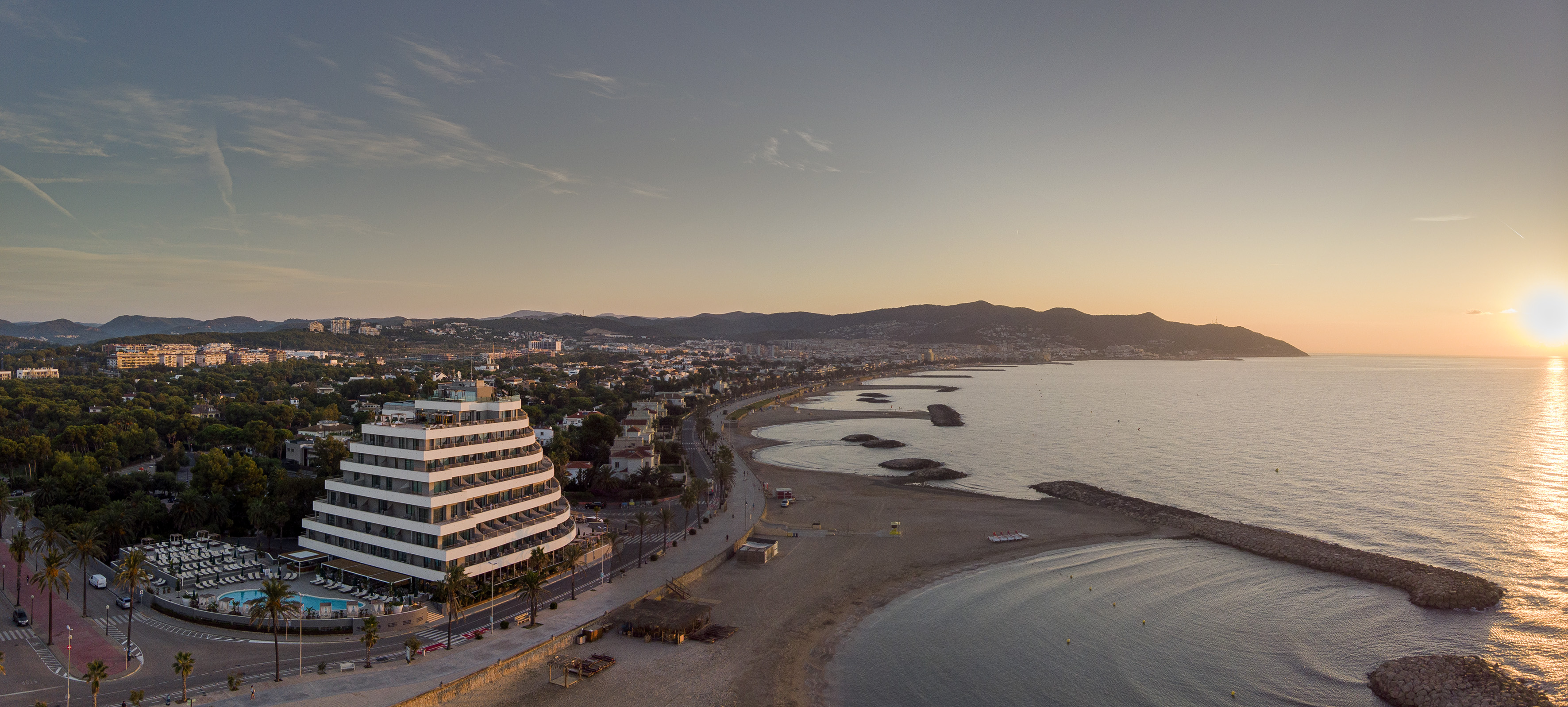 Aerial view: Modern coastal resort hotel, beach, and sunrise over ocean.
