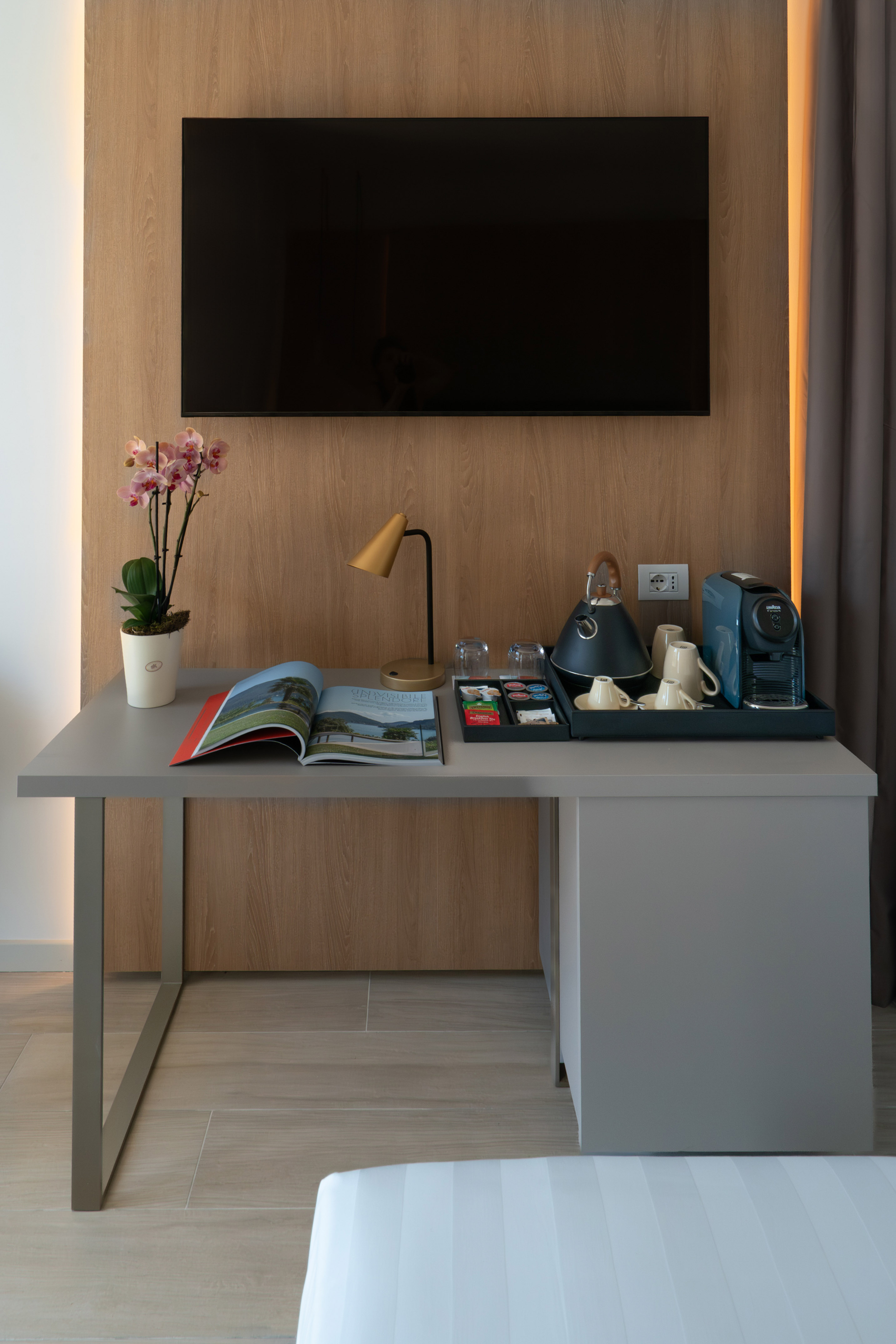 Modern hotel room with TV, desk, coffee maker, kettle, and amenities.