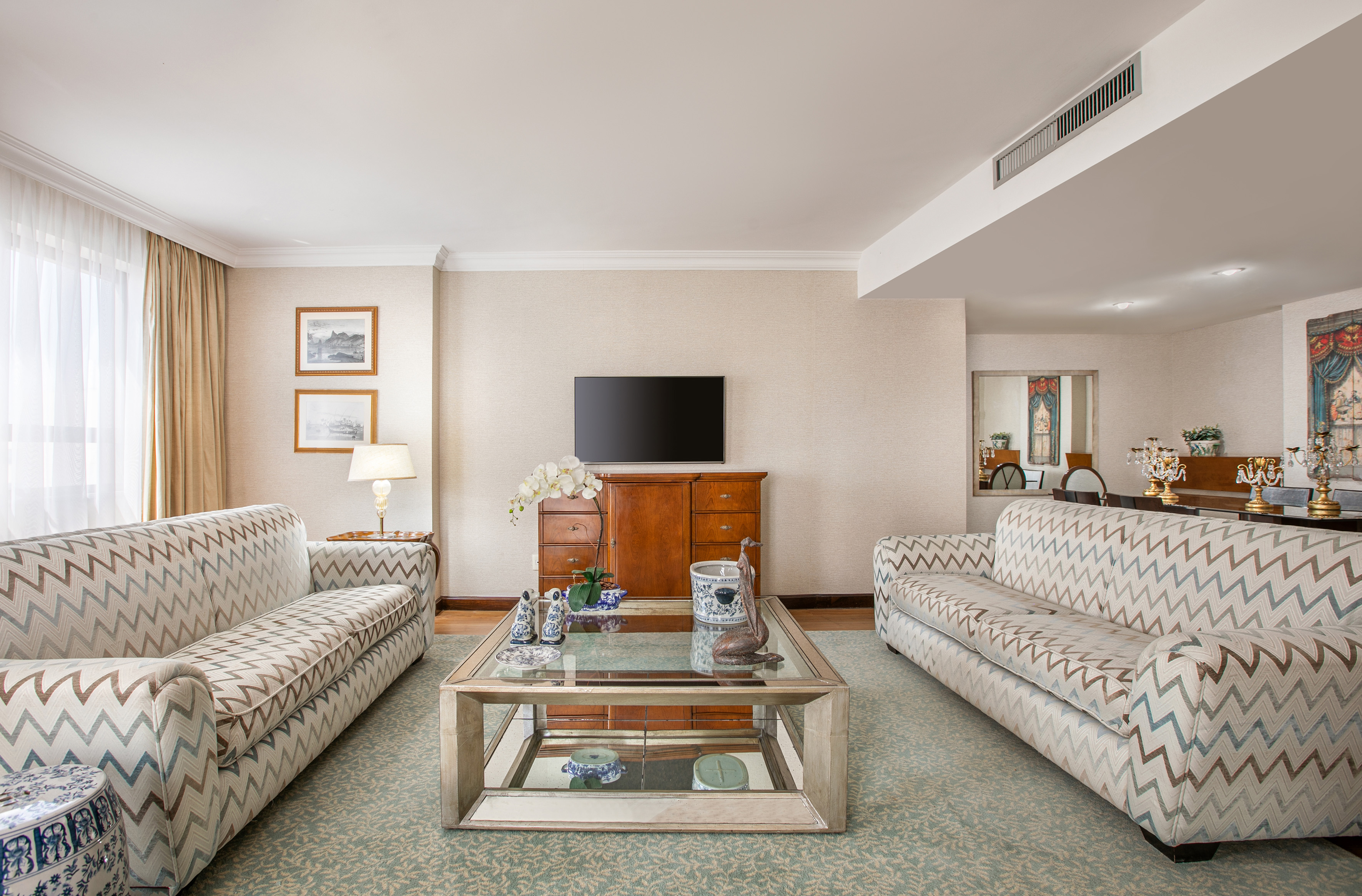 Bright living room with chevron sofas, mirrored coffee table, TV, and dining view.