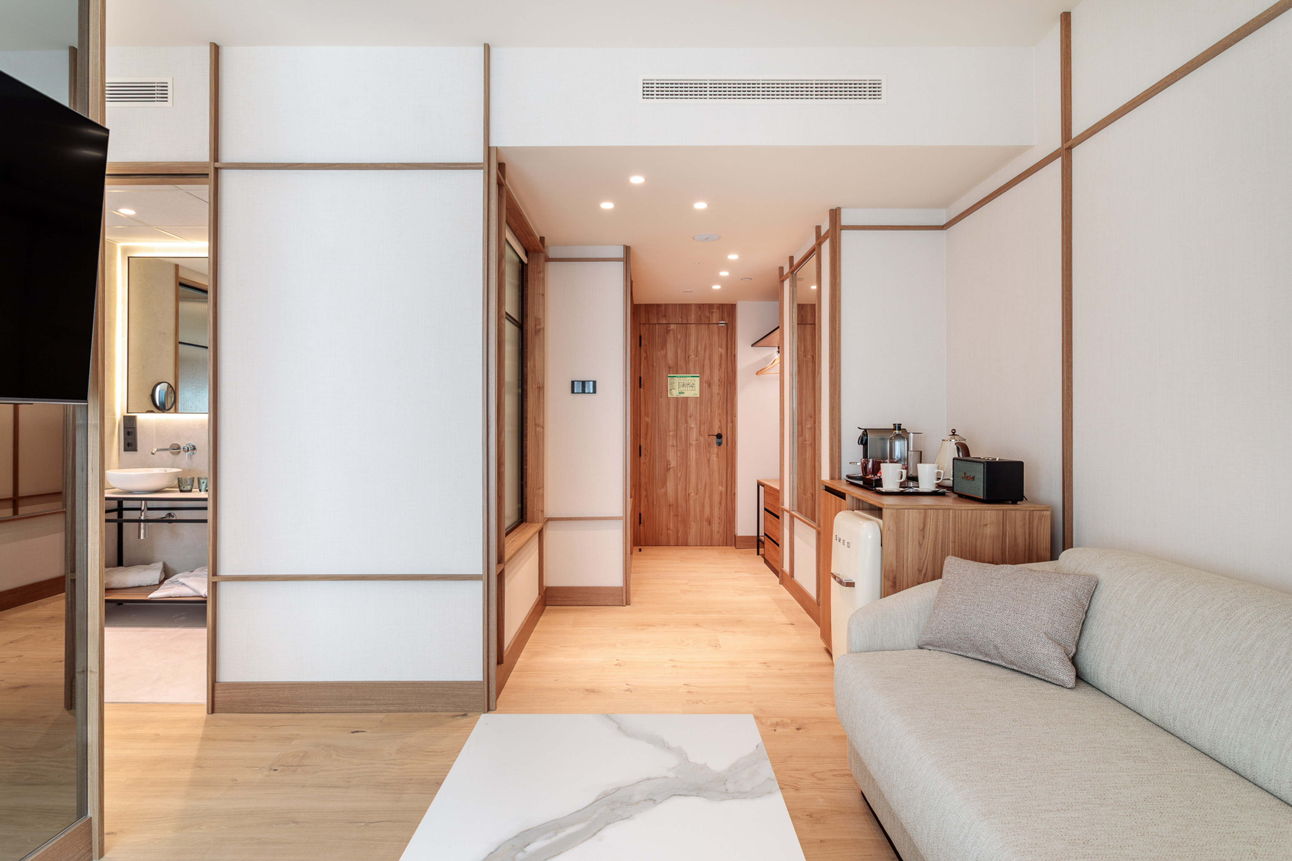 Modern hotel suite with sofa, coffee table, wood floor, and kitchenette.