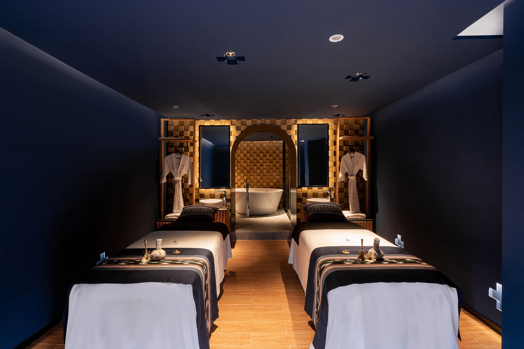 Luxury spa room with two massage beds, dark blue decor, and bathtub.