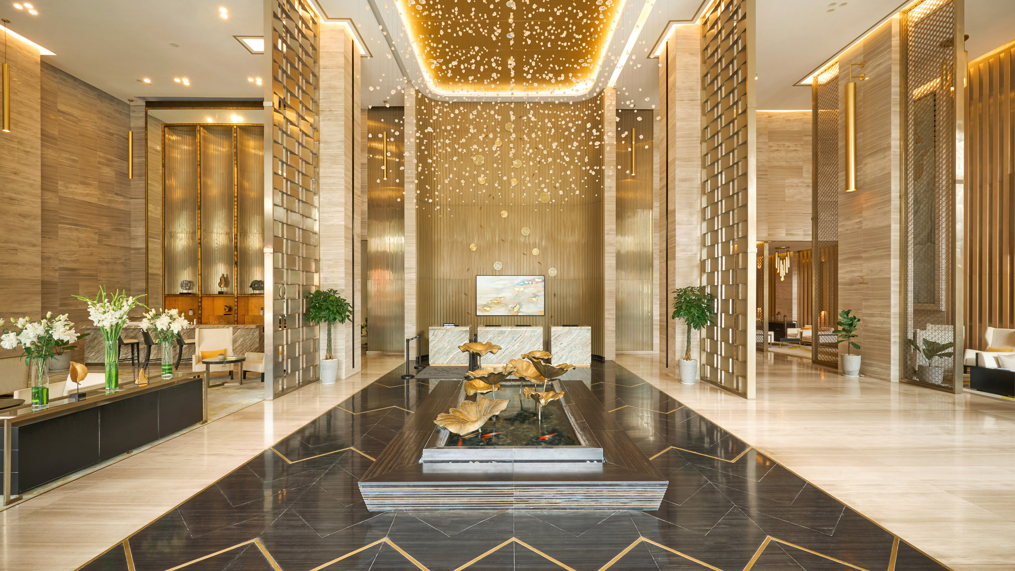 Luxury hotel lobby with gold chandelier, marble floors, and lotus fountain.