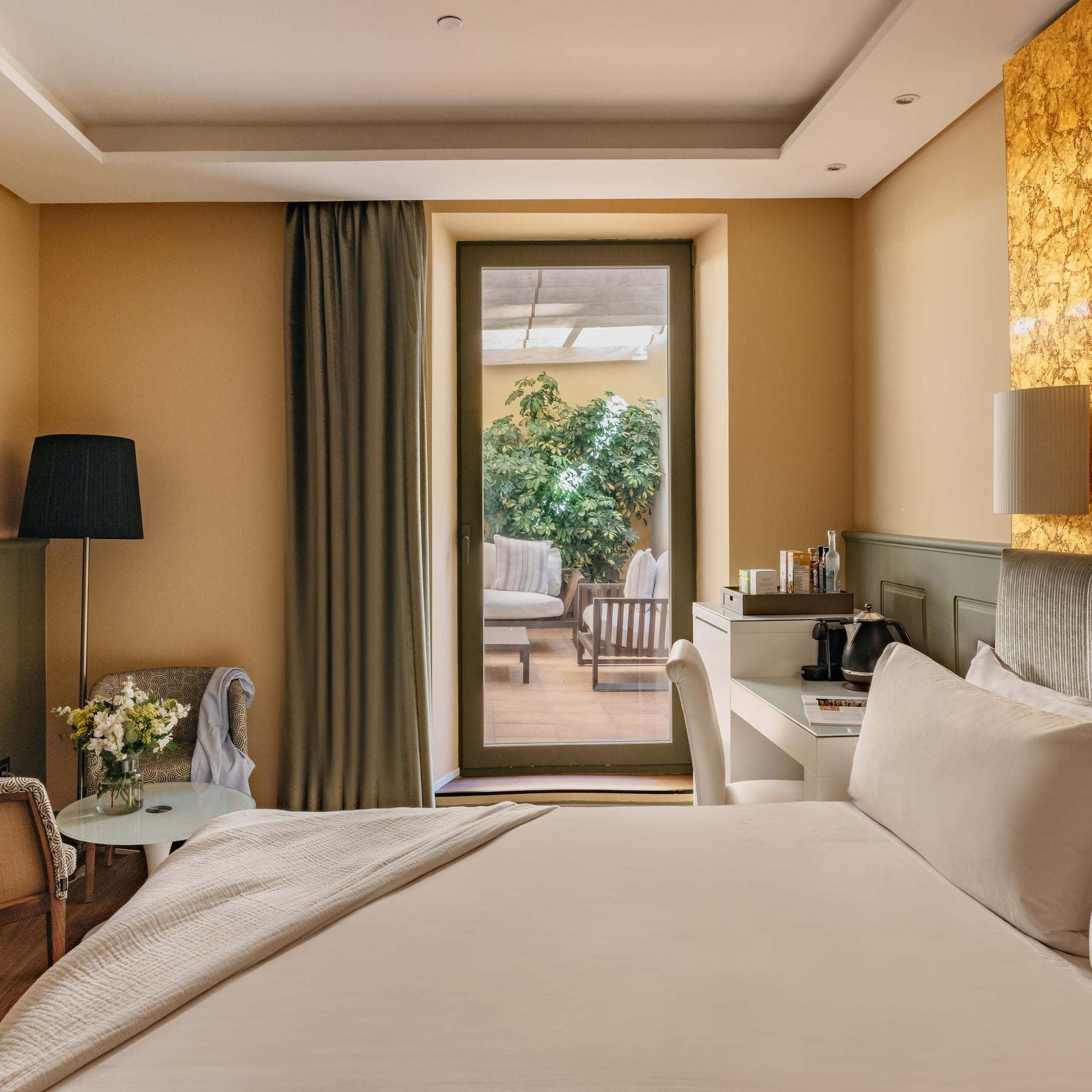 Habitación de hotel moderna, cama, balcón a terraza y pared dorada.