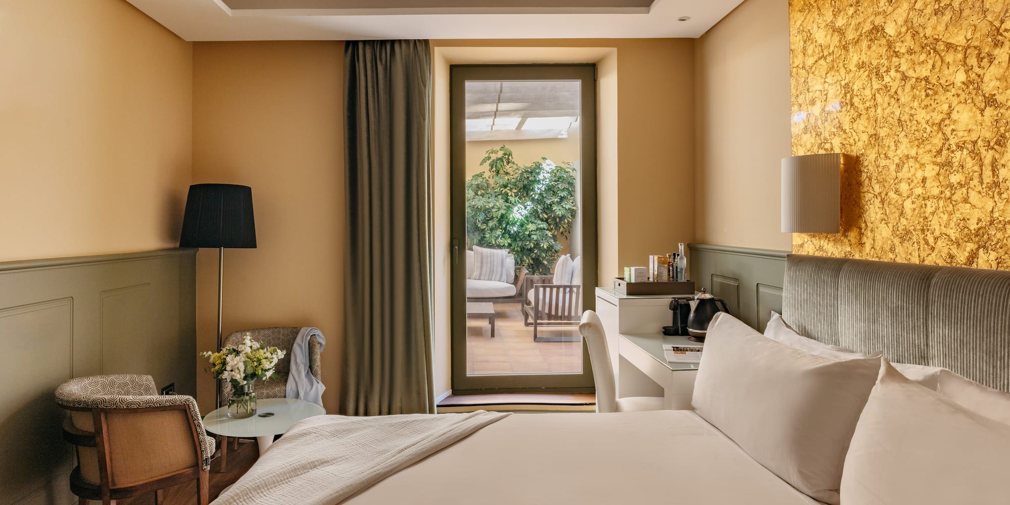 Habitación de hotel moderna, cama, balcón a terraza y pared dorada.