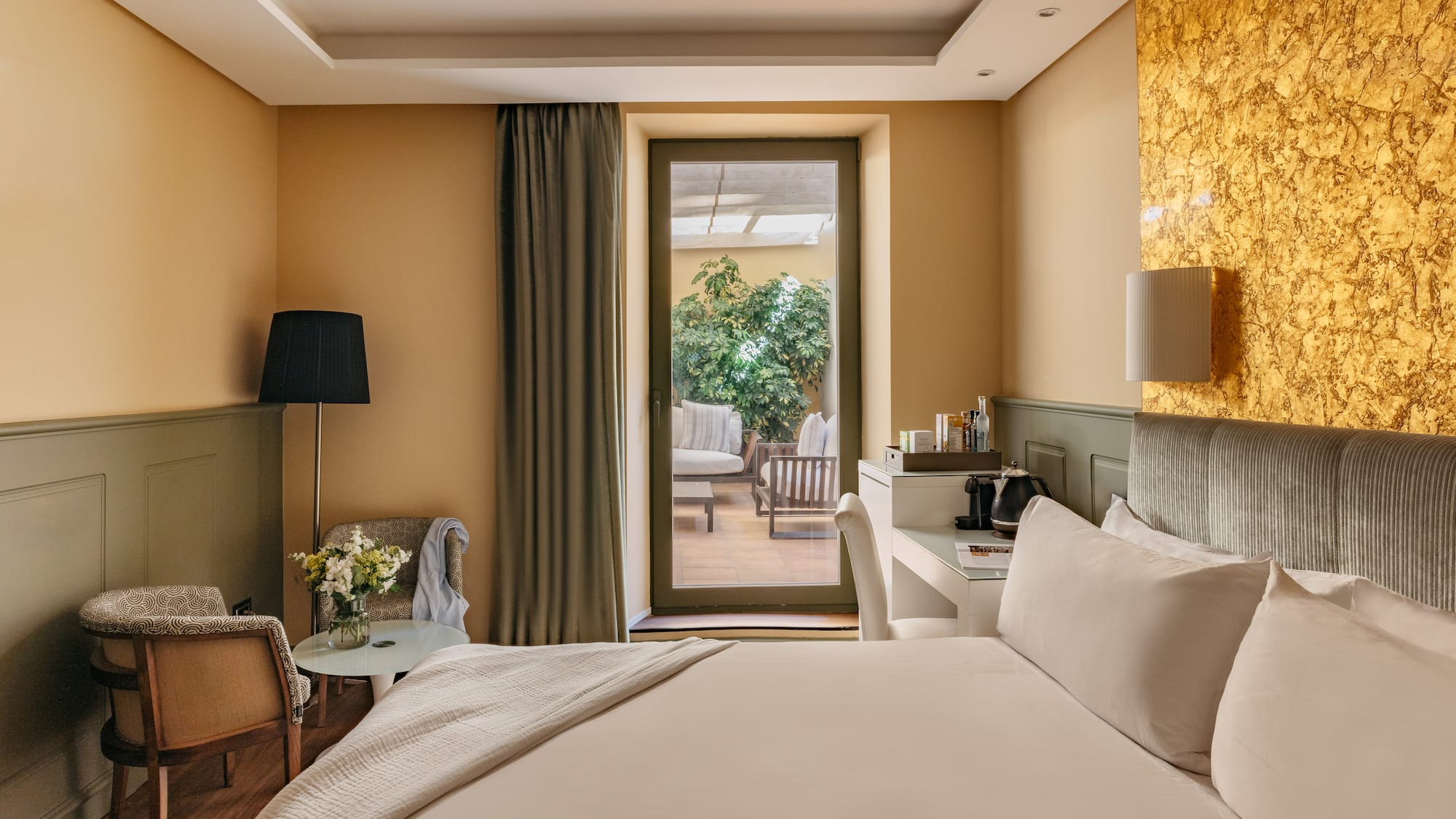 Habitación de hotel moderna, cama, balcón a terraza y pared dorada.
