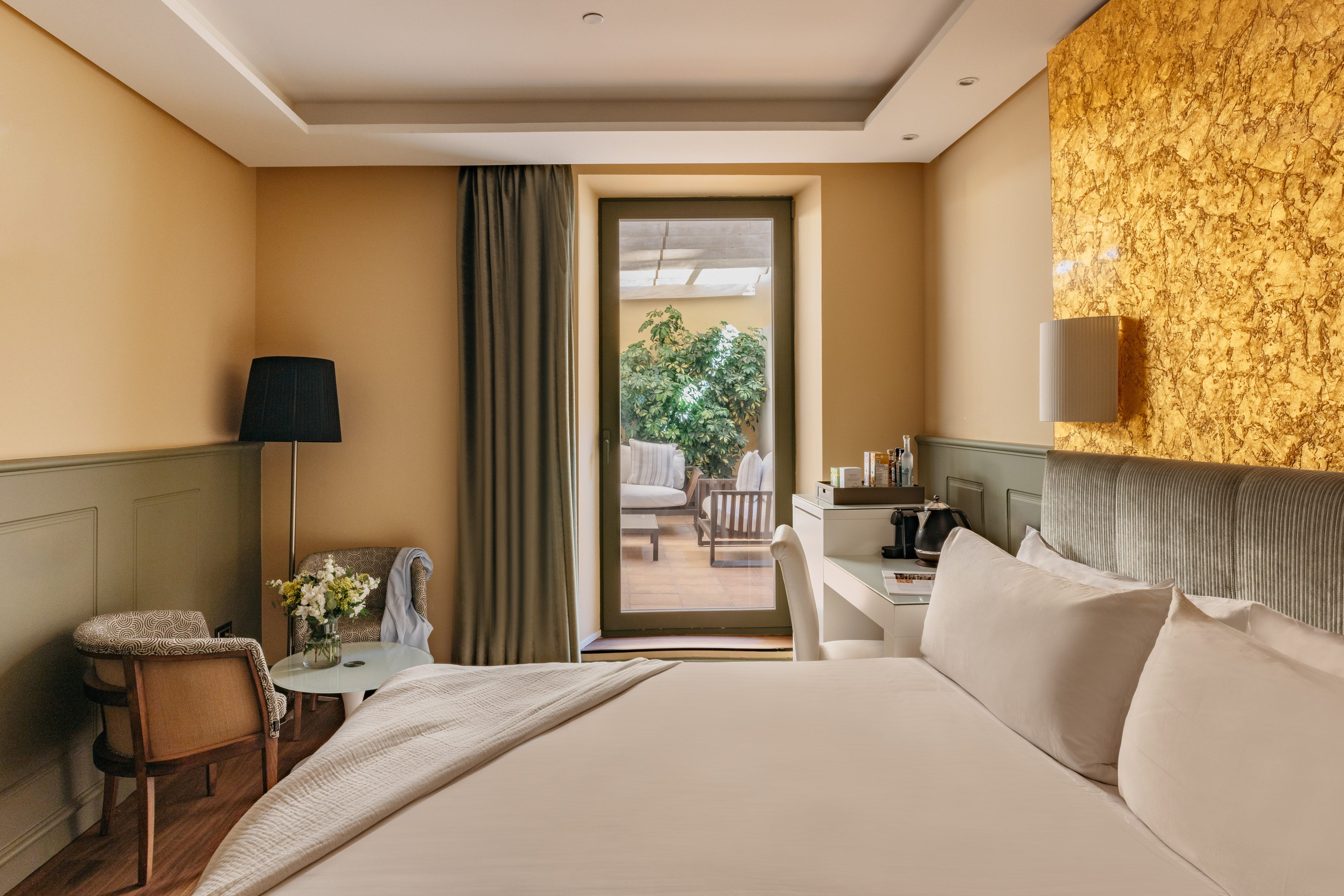 Habitación de hotel moderna, cama, balcón a terraza y pared dorada.