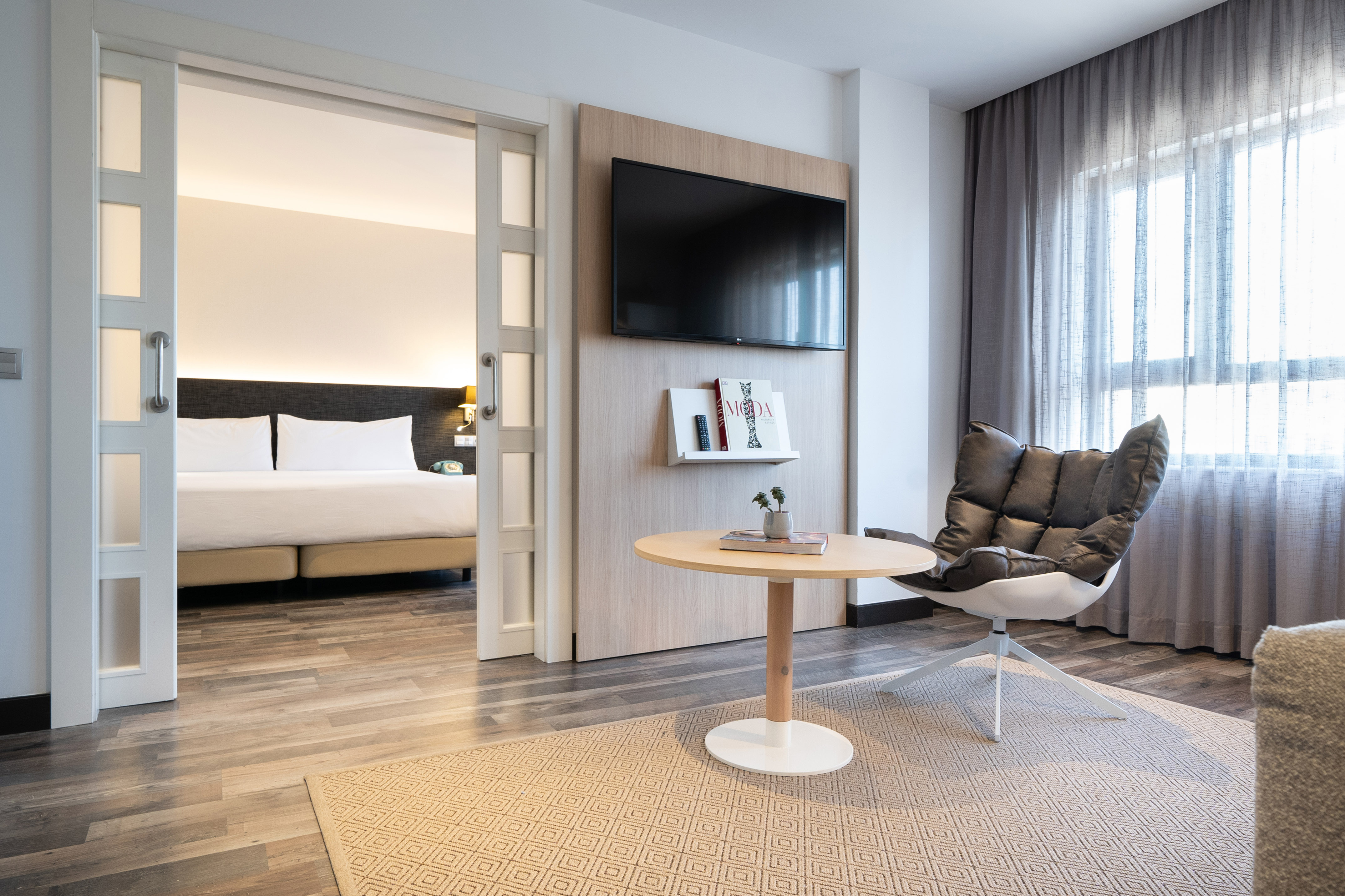 Modern hotel suite living area with flat-screen TV and open bedroom.