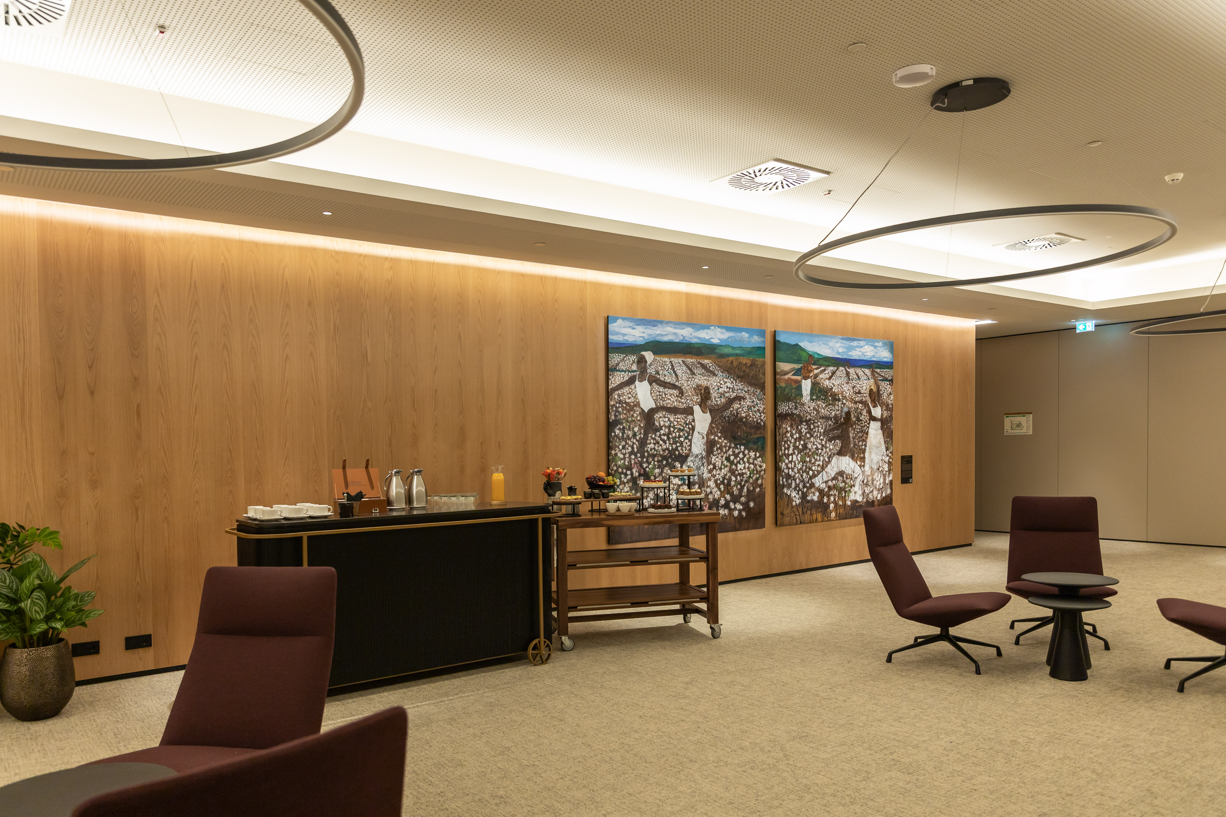Modern hotel lounge with wood walls, art, coffee bar, and maroon chairs.