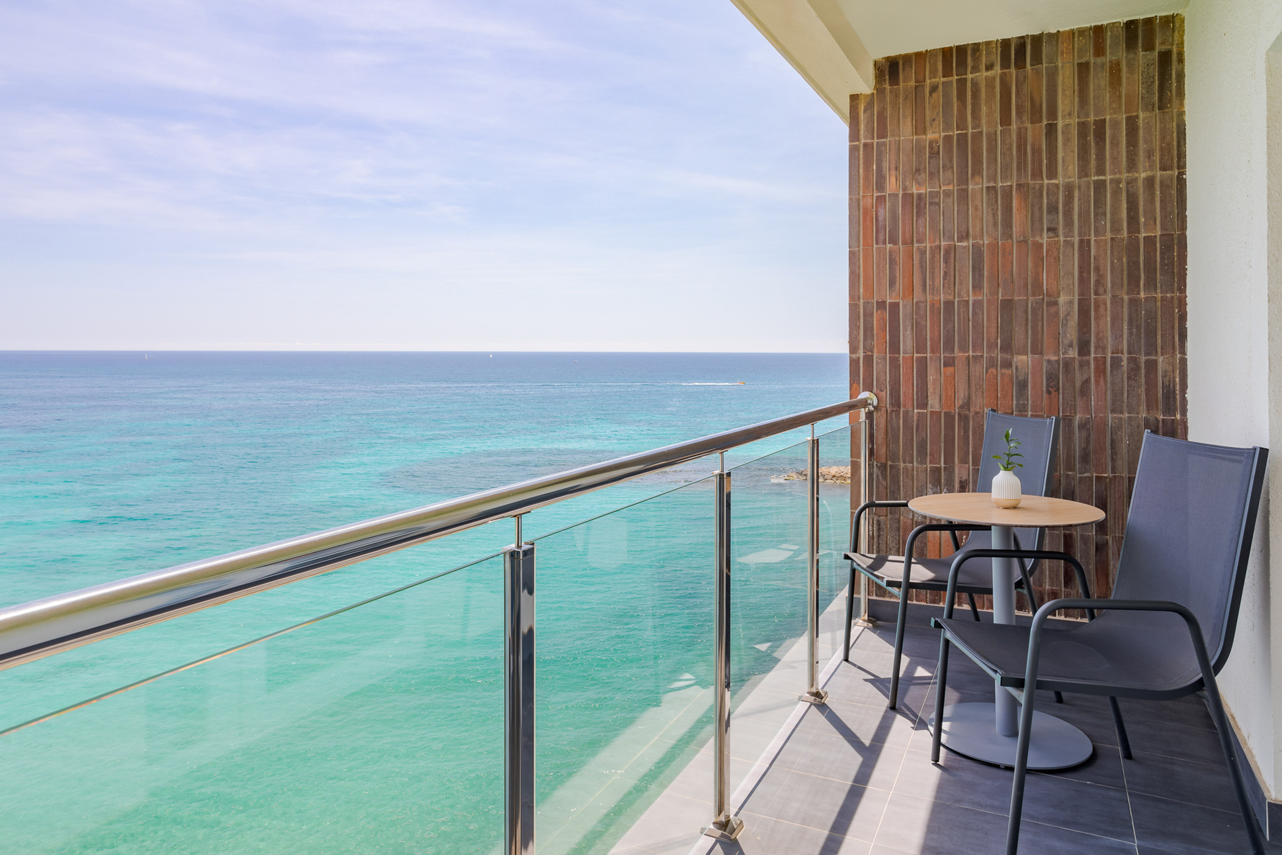 Ocean view balcony with turquoise water, outdoor table and chairs.