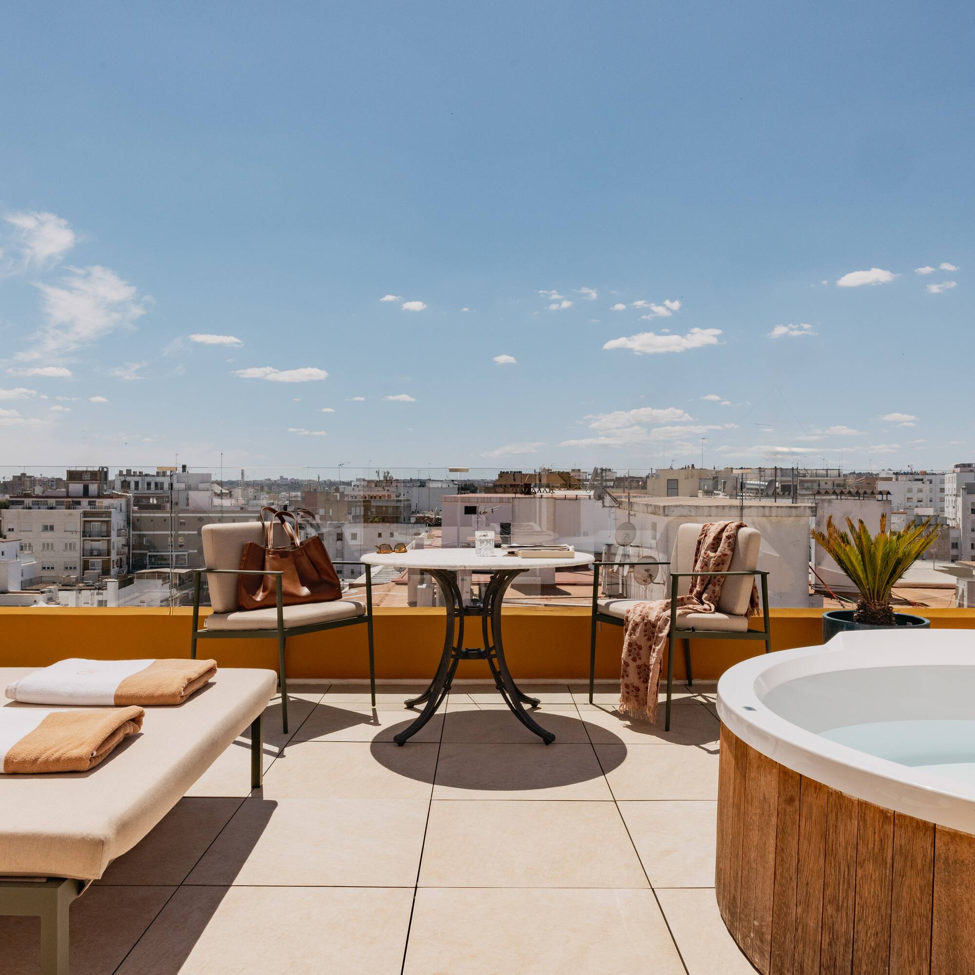 Azotea moderna con jacuzzi, tumbona y vistas a la ciudad bajo cielo azul.