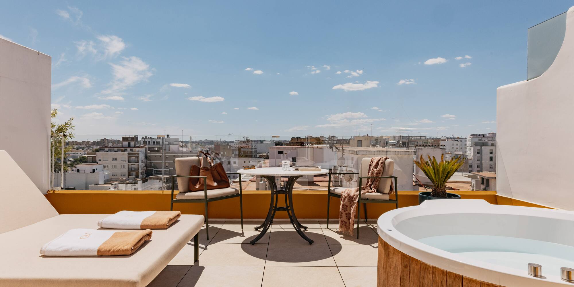 Azotea moderna con jacuzzi, tumbona y vistas a la ciudad bajo cielo azul.