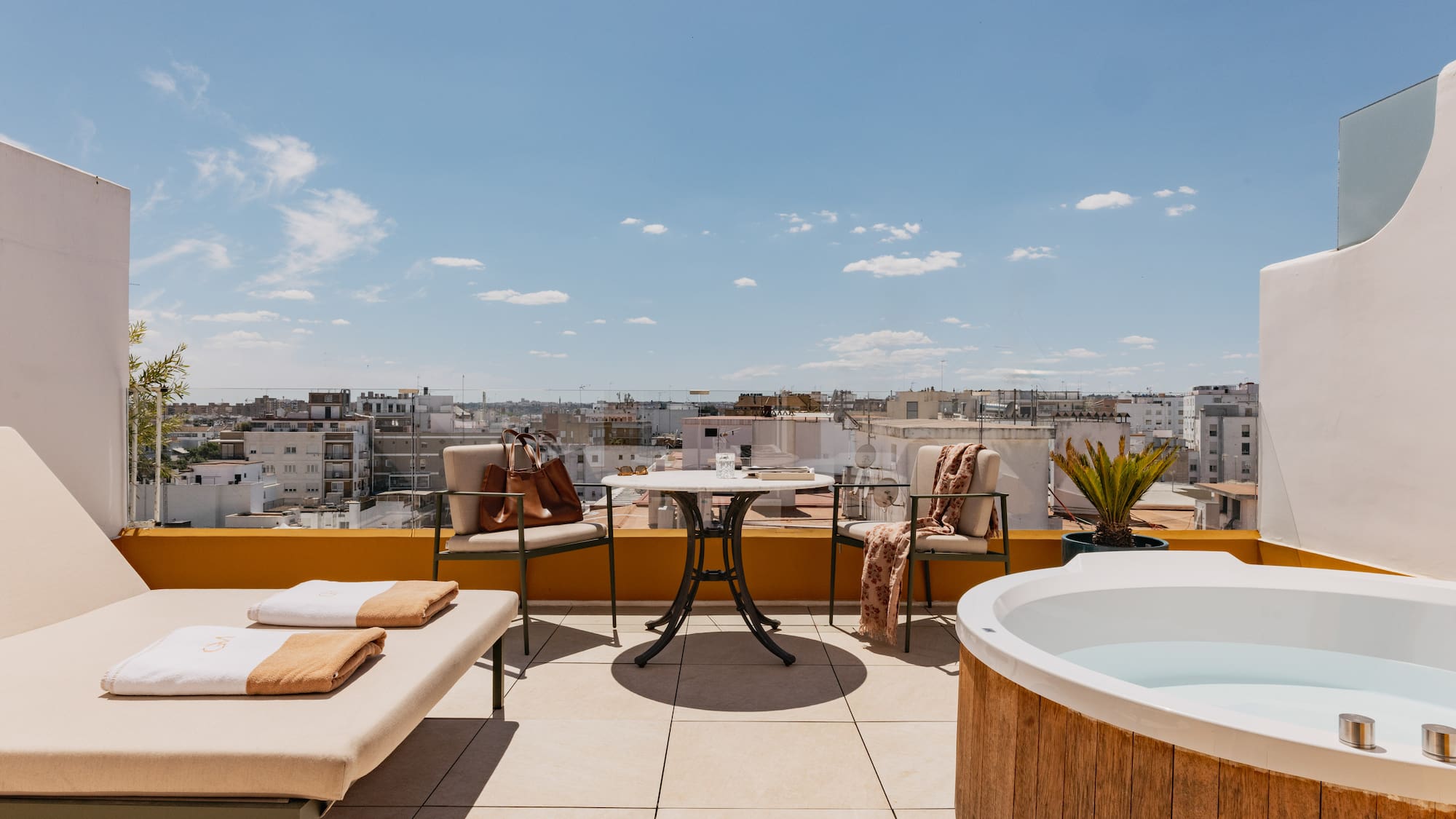 Azotea moderna con jacuzzi, tumbona y vistas a la ciudad bajo cielo azul.