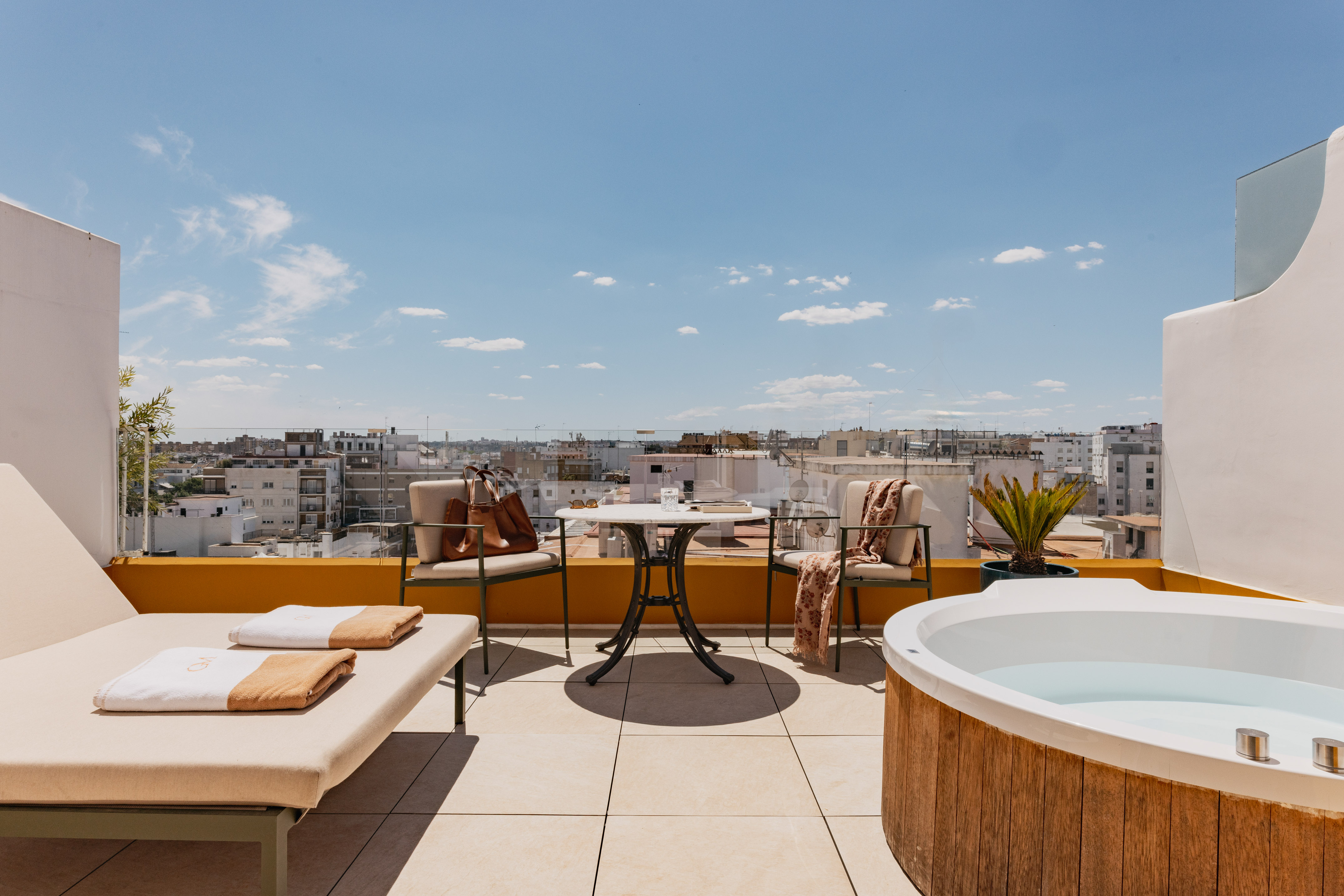 Azotea moderna con jacuzzi, tumbona y vistas a la ciudad bajo cielo azul.