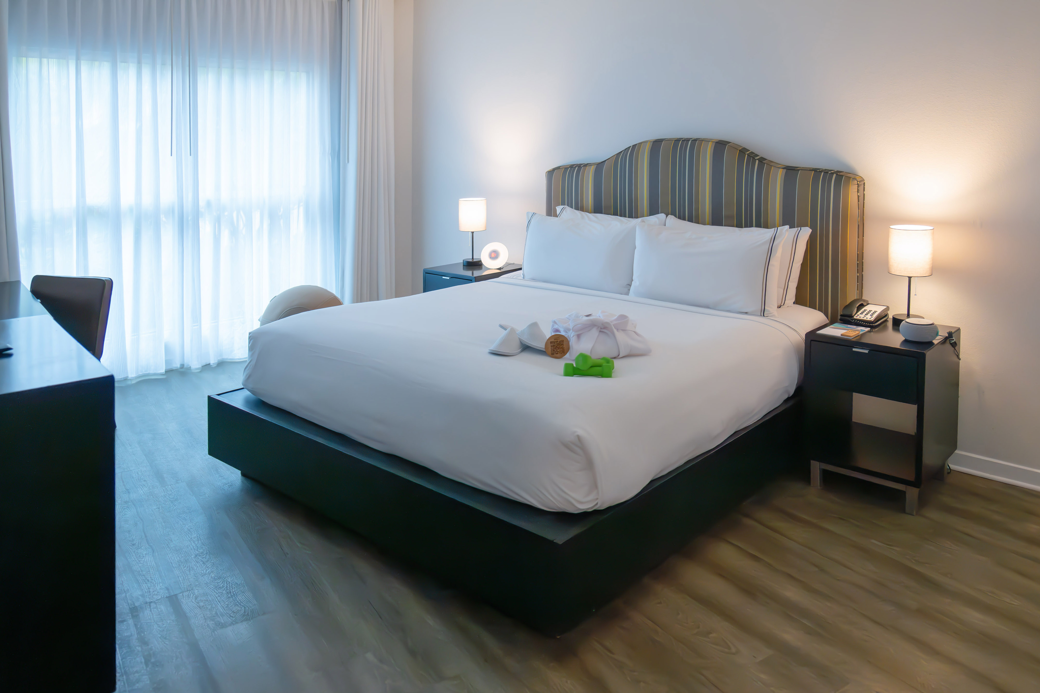 Modern hotel bedroom with king bed, white linens, wellness amenities, and sleek decor.