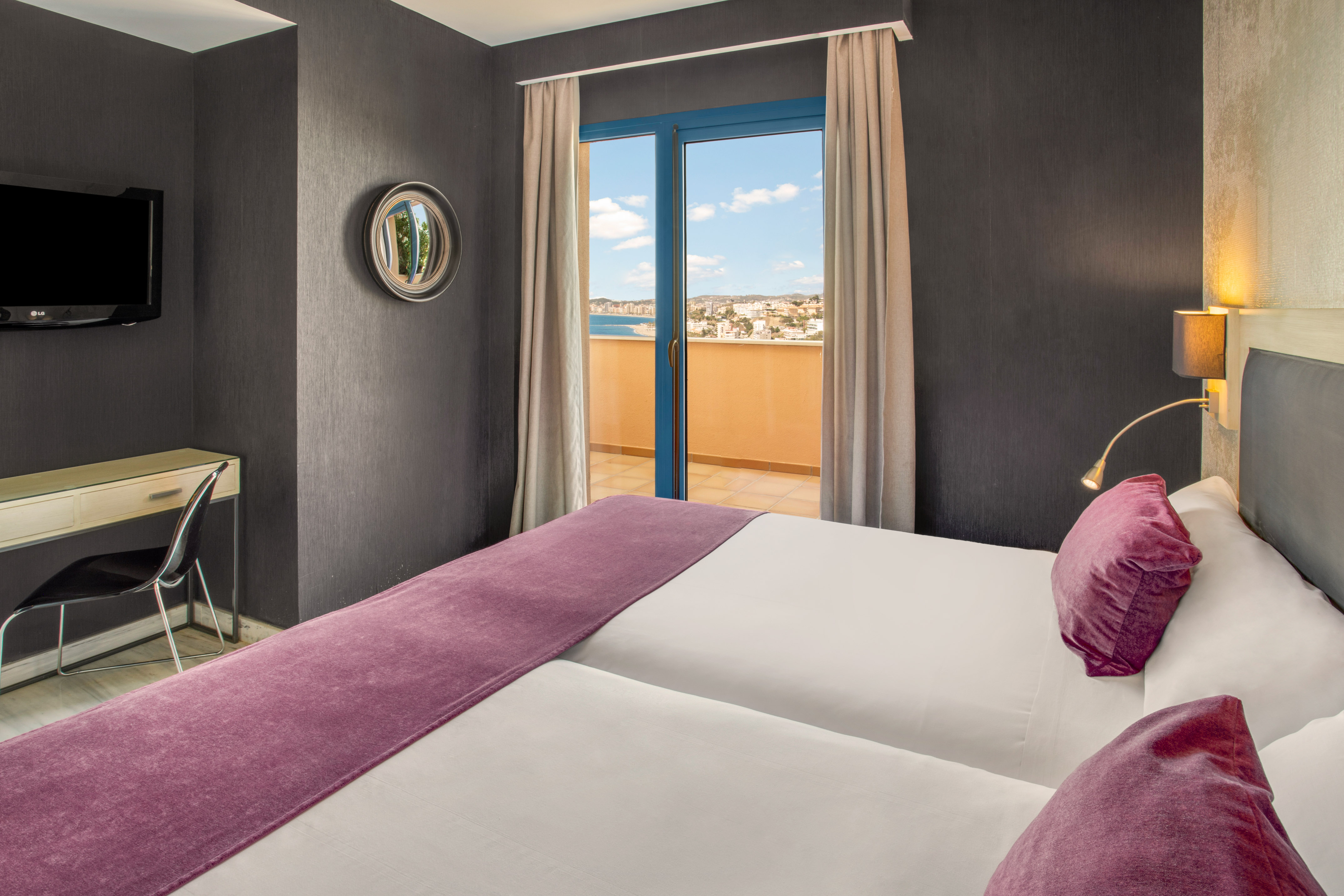 Modern hotel room with balcony sea view, twin beds, and purple decor.