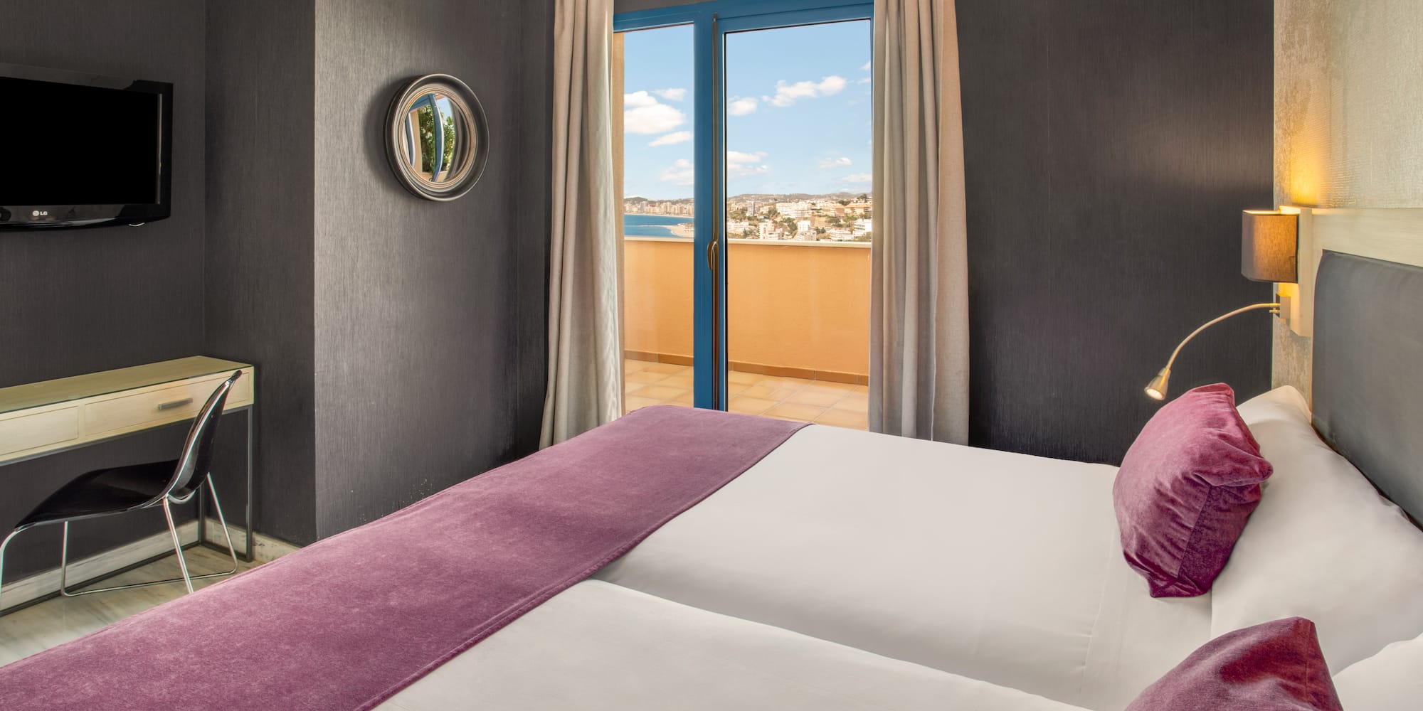 Modern hotel room with balcony sea view, twin beds, and purple decor.