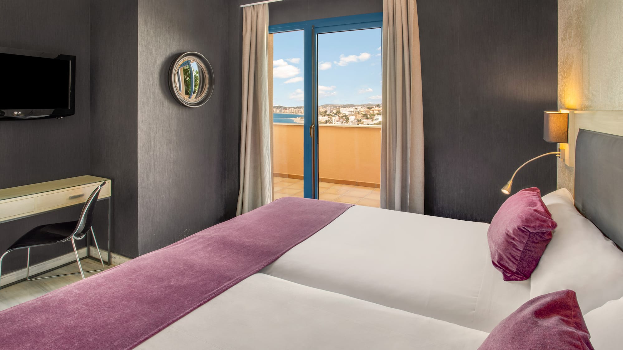 Modern hotel room with balcony sea view, twin beds, and purple decor.