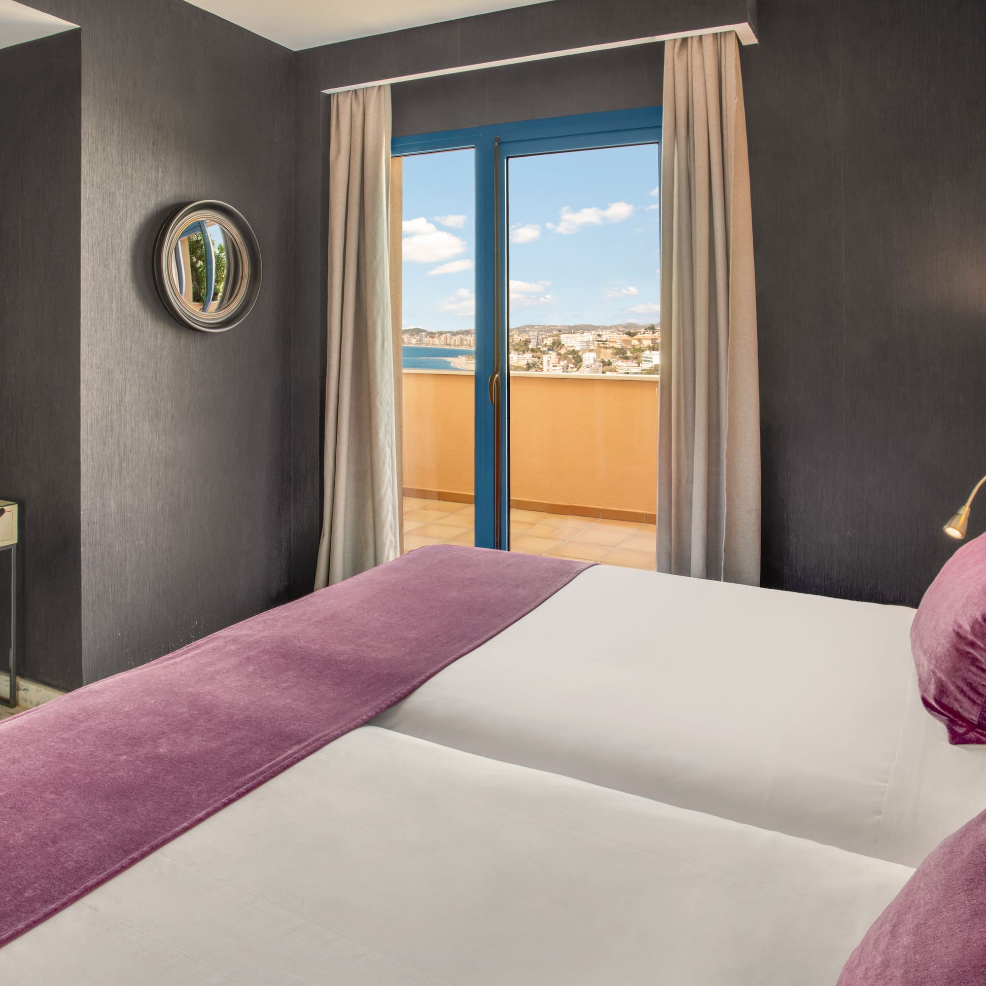 Modern hotel room with balcony sea view, twin beds, and purple decor.