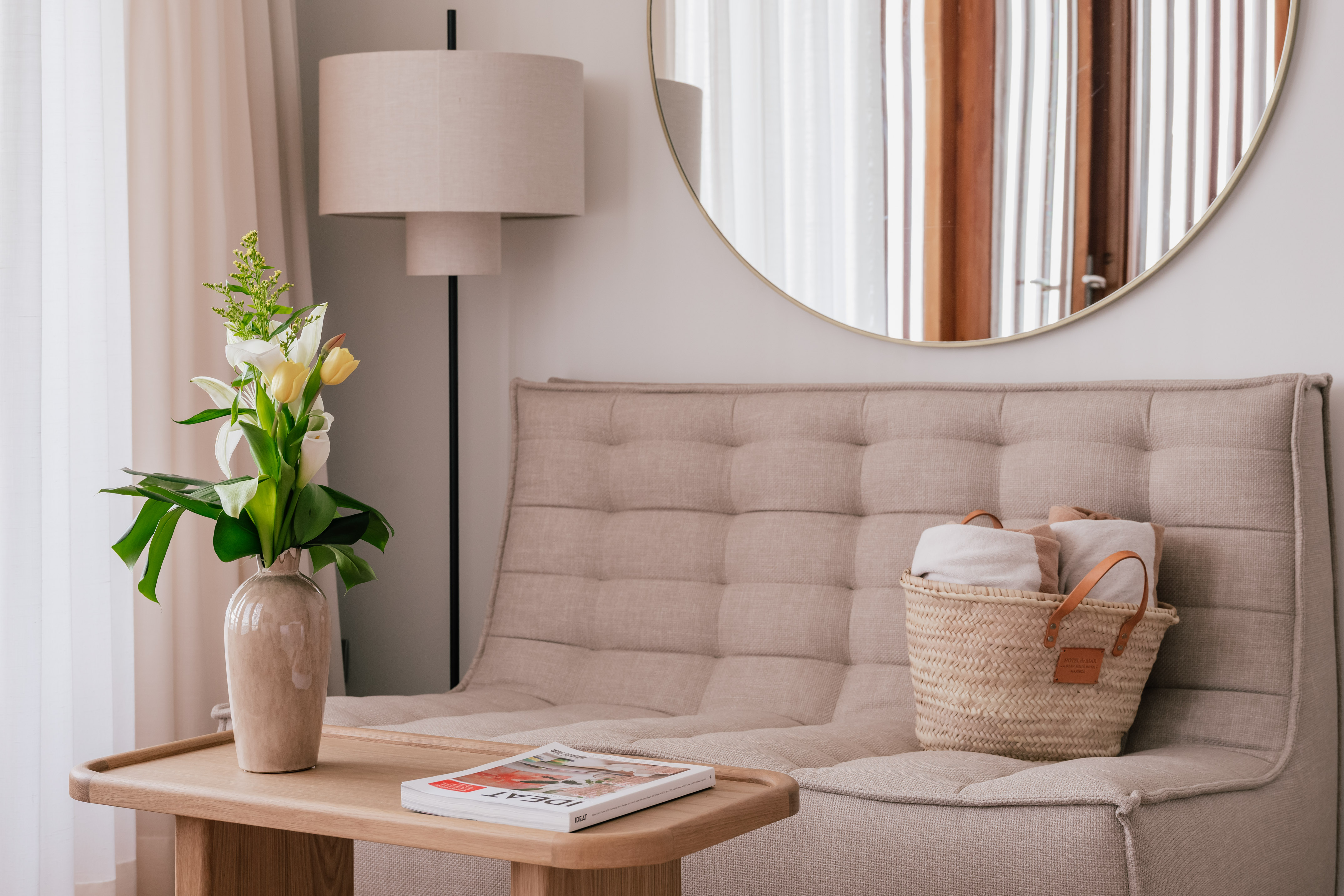 Modern living room with beige sofa, coffee table, fresh flowers, mirror, and floor lamp.