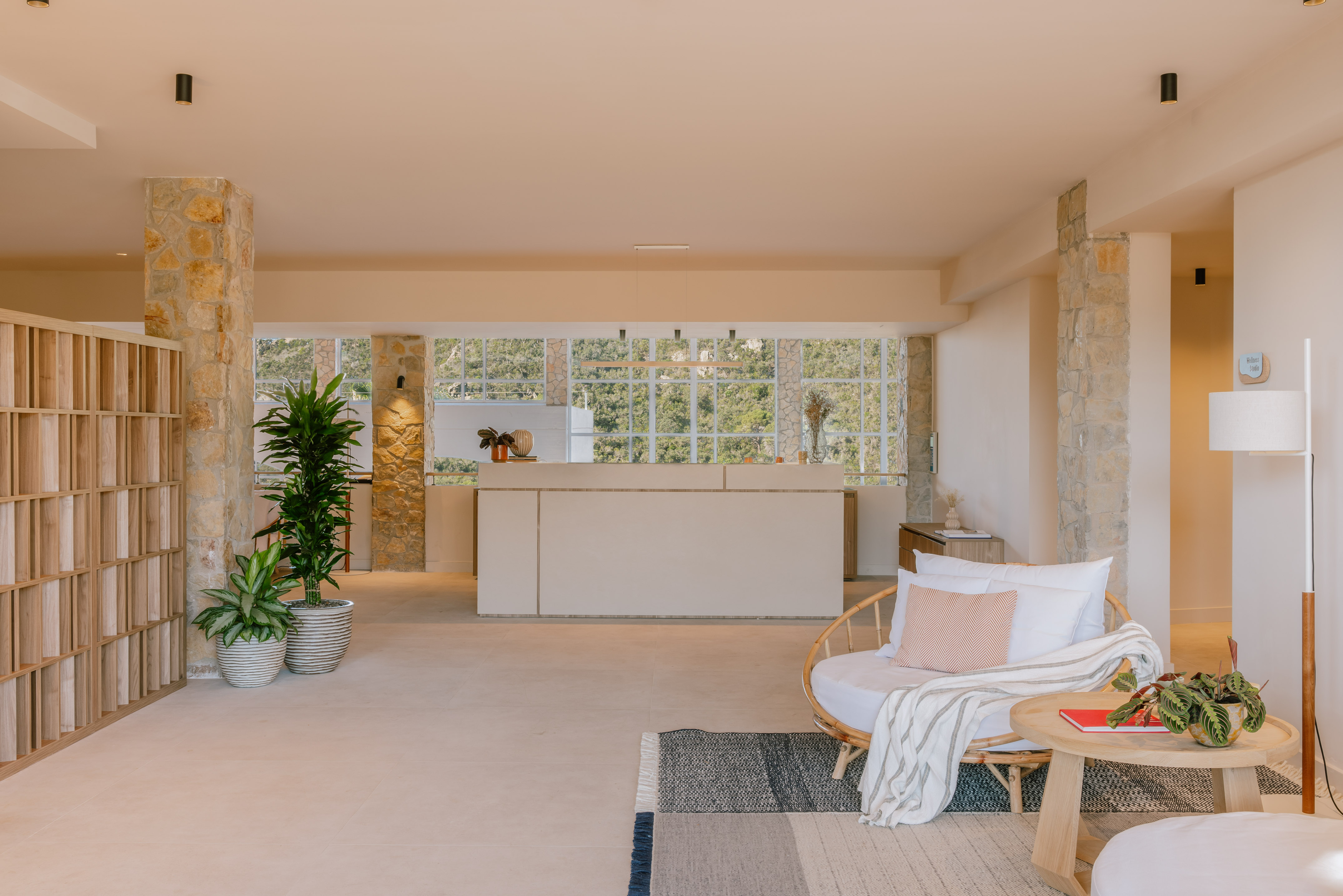 Modern open-plan living room with stone pillars, kitchen, windows, wicker chair.