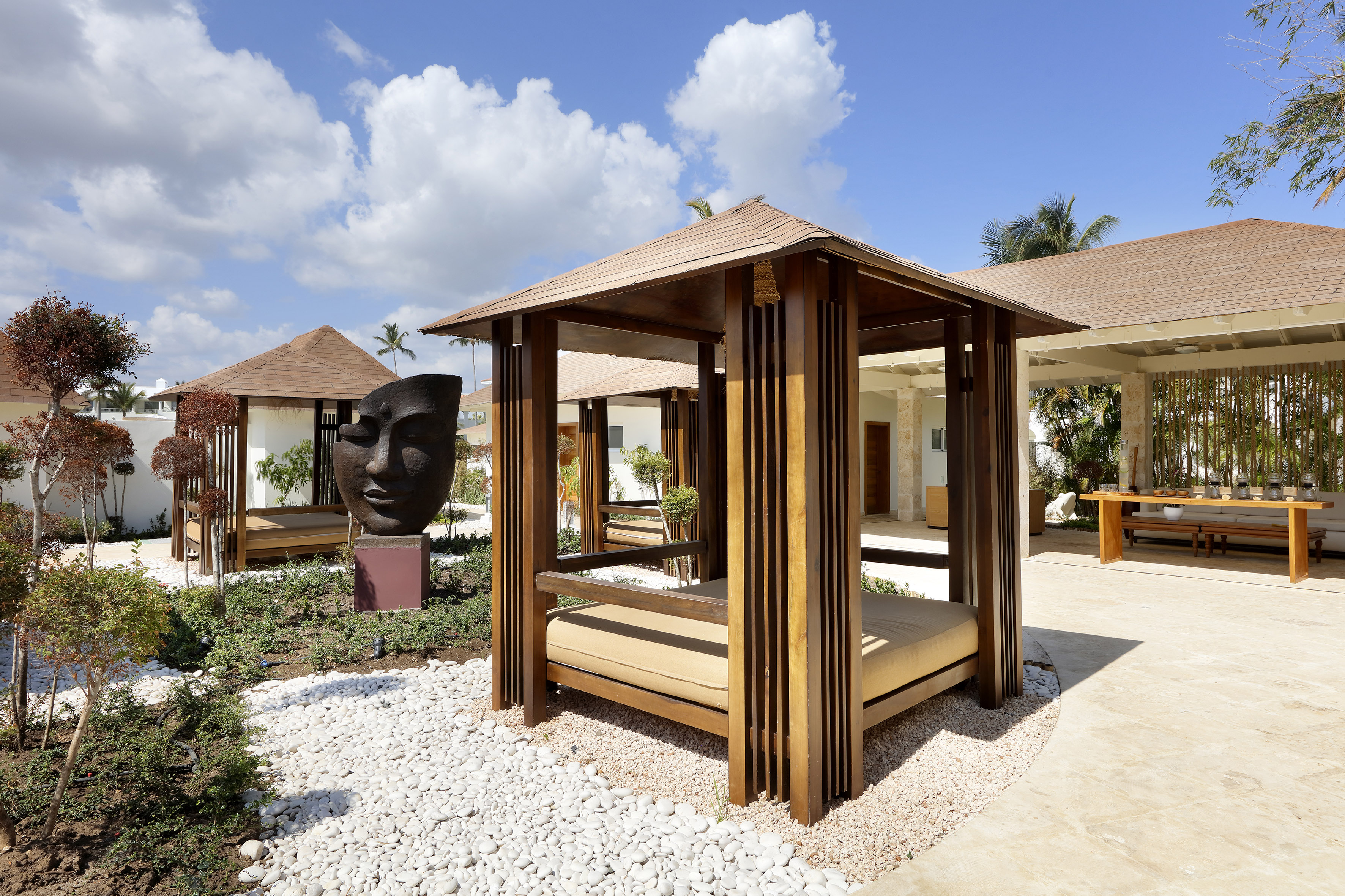 Outdoor wooden cabanas with daybeds in a tropical garden with mask sculpture.