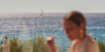 a woman sitting at a table with a sailboat in the background