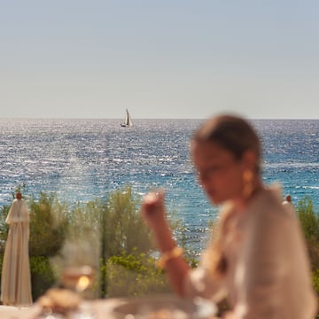 a woman sitting at a table with a sailboat in the background