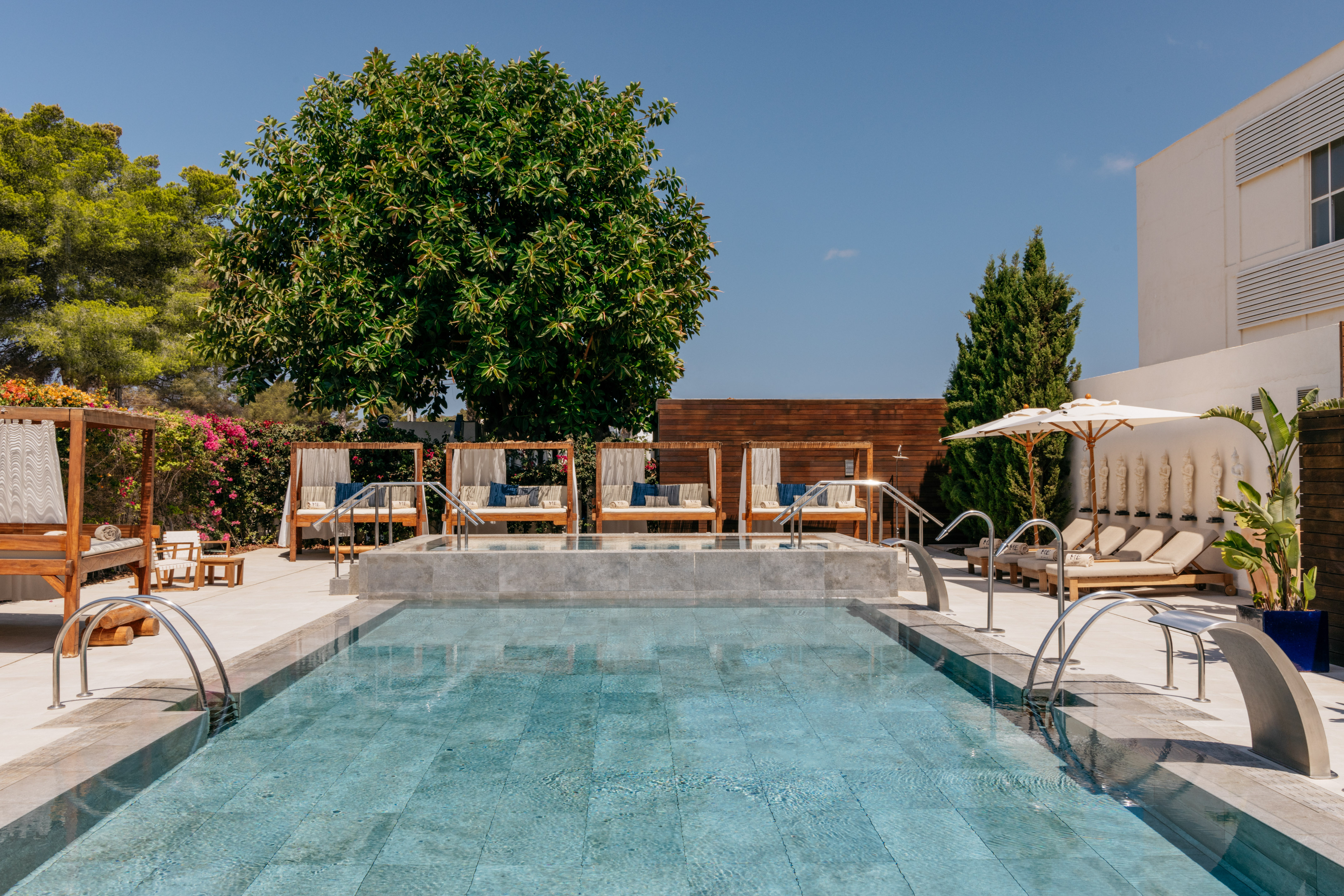Luxury resort swimming pool with cabanas, sun loungers, and green trees.