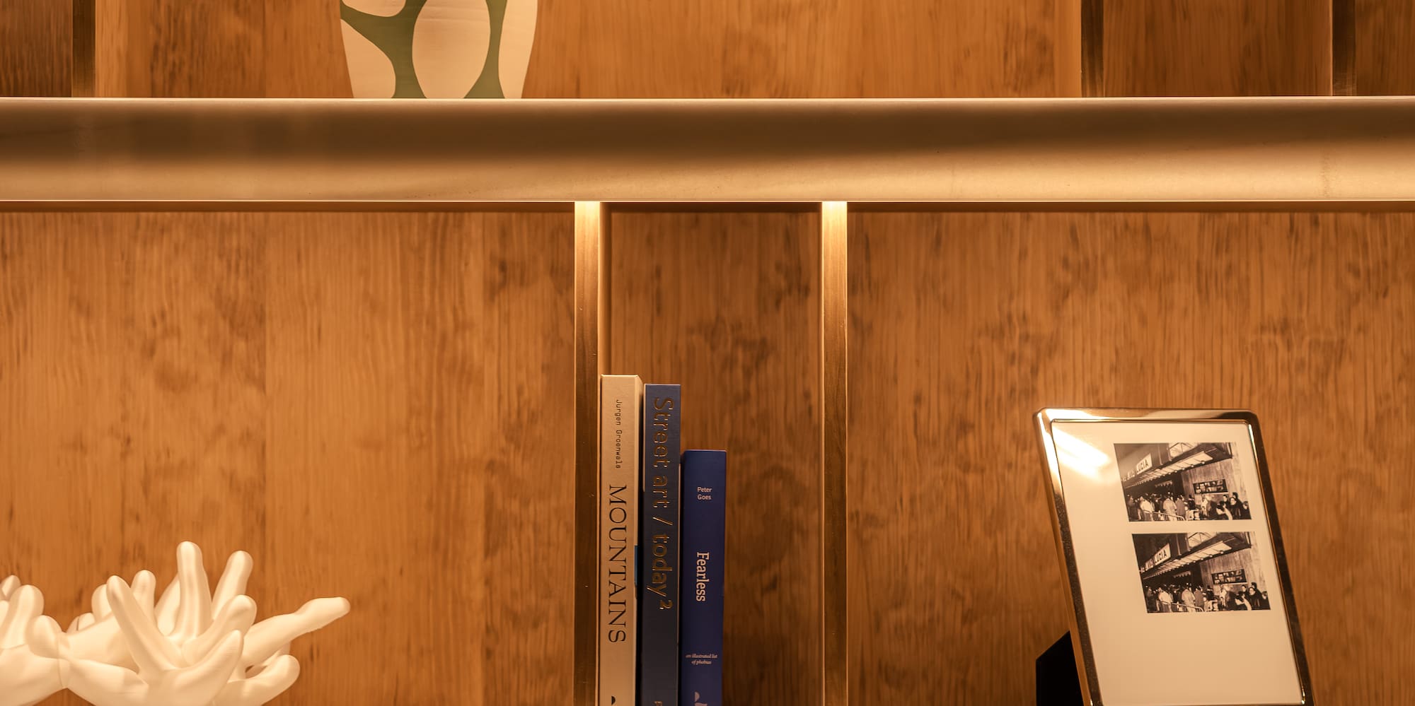 Illuminated wooden display shelves with books, art objects, and framed photos.