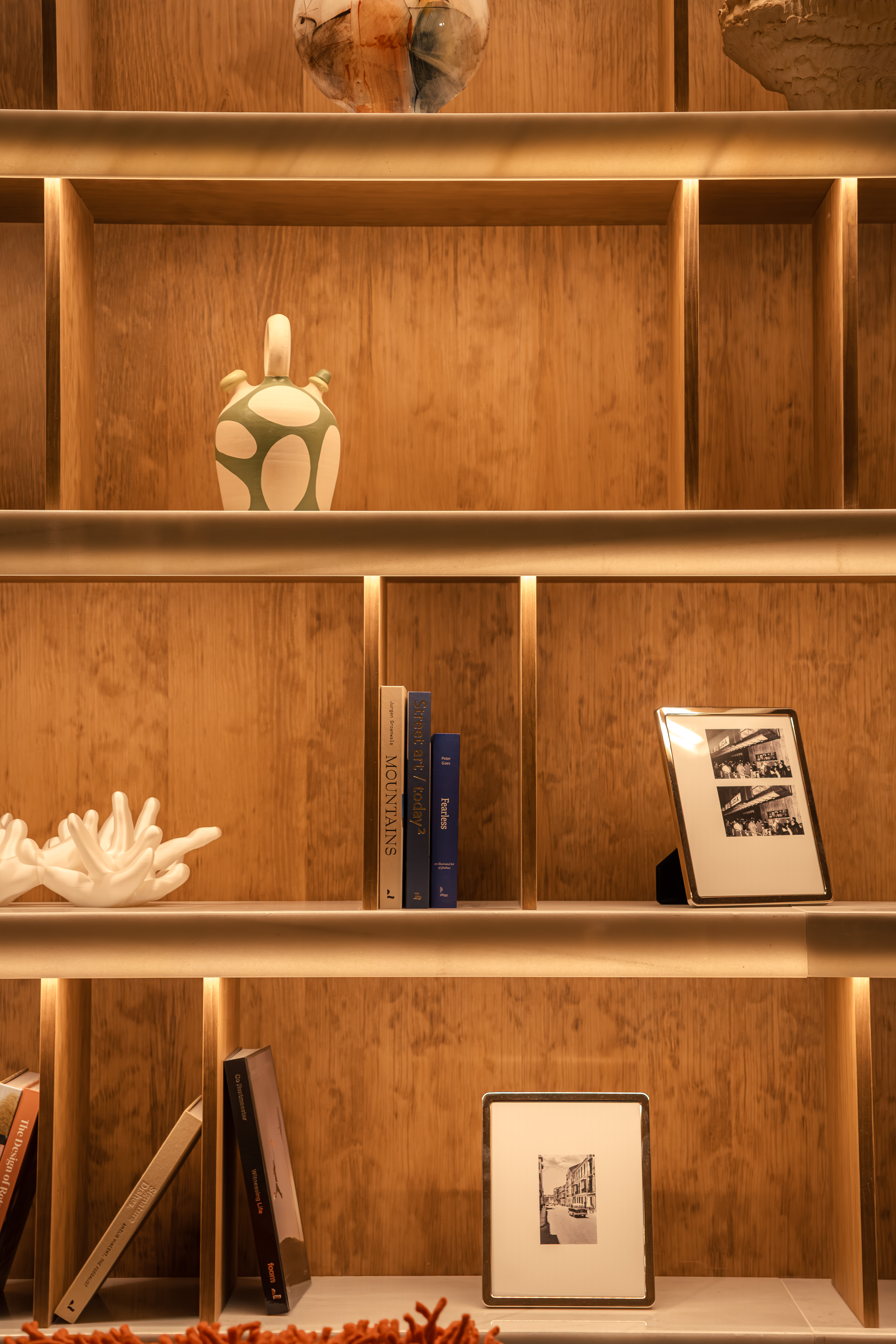 Illuminated wooden display shelves with books, art objects, and framed photos.