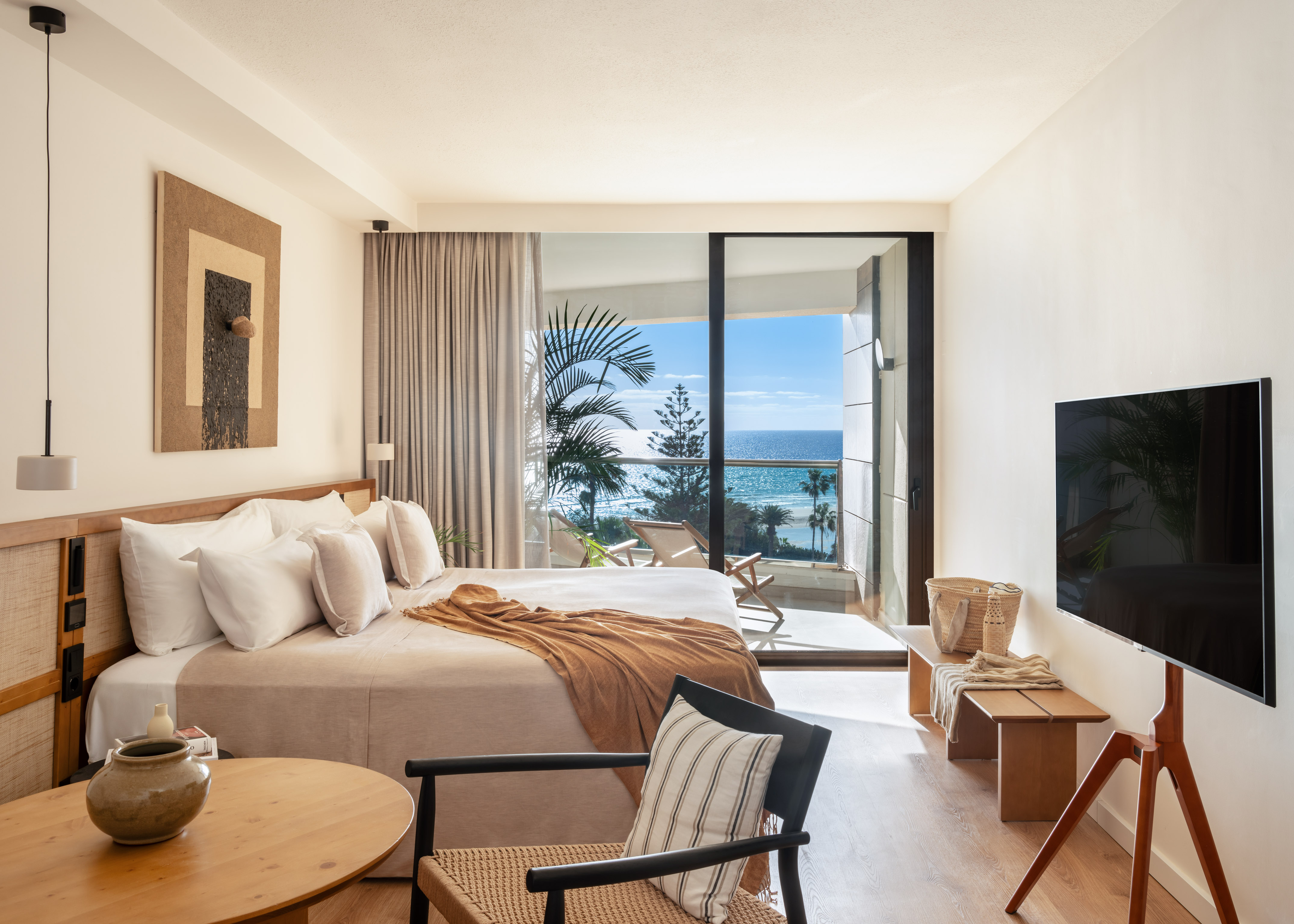 Beachfront hotel room with modern decor, large bed, and ocean view balcony.