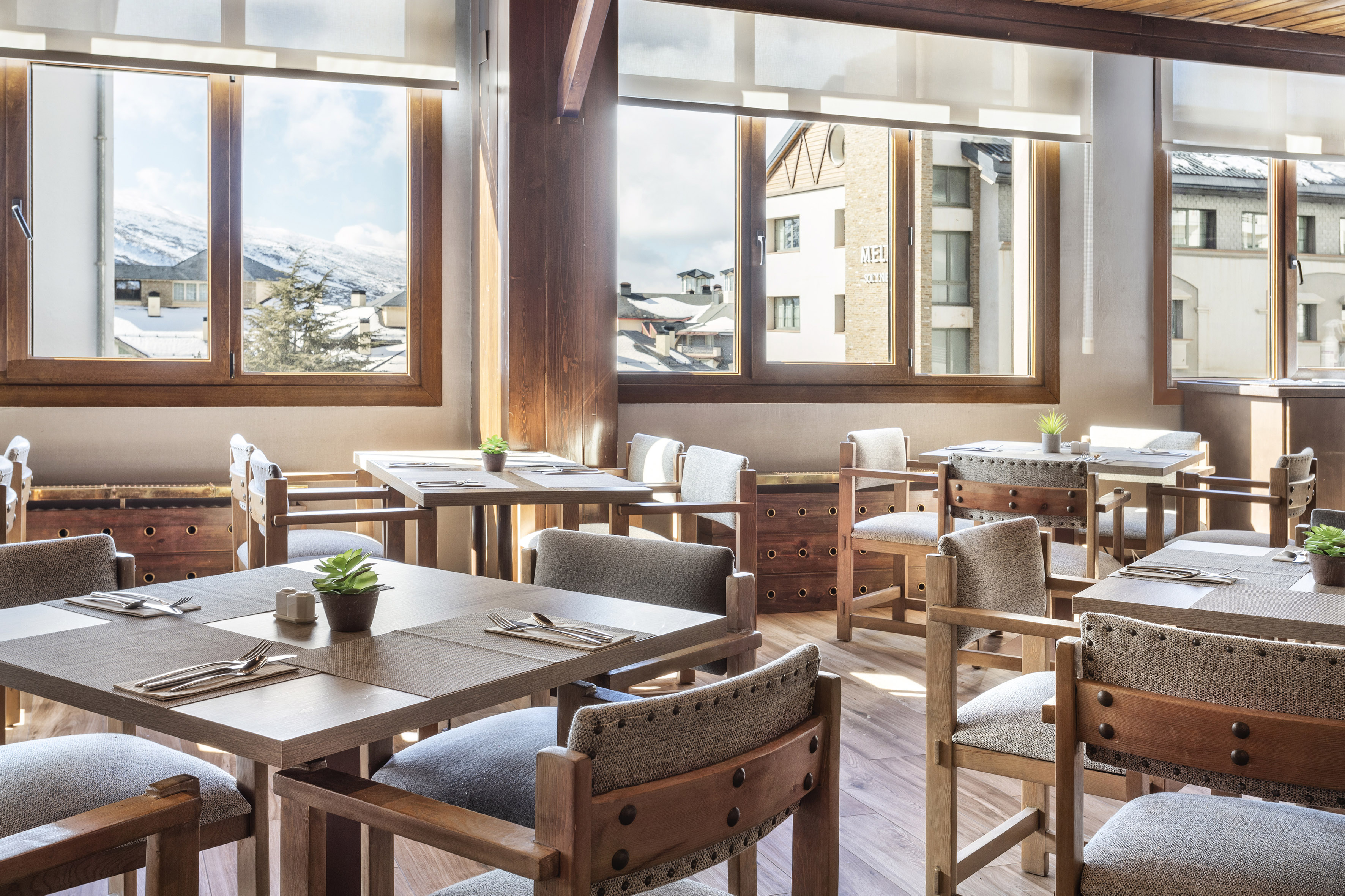 Restaurant interior with wooden tables, chairs, and snowy mountain window view.