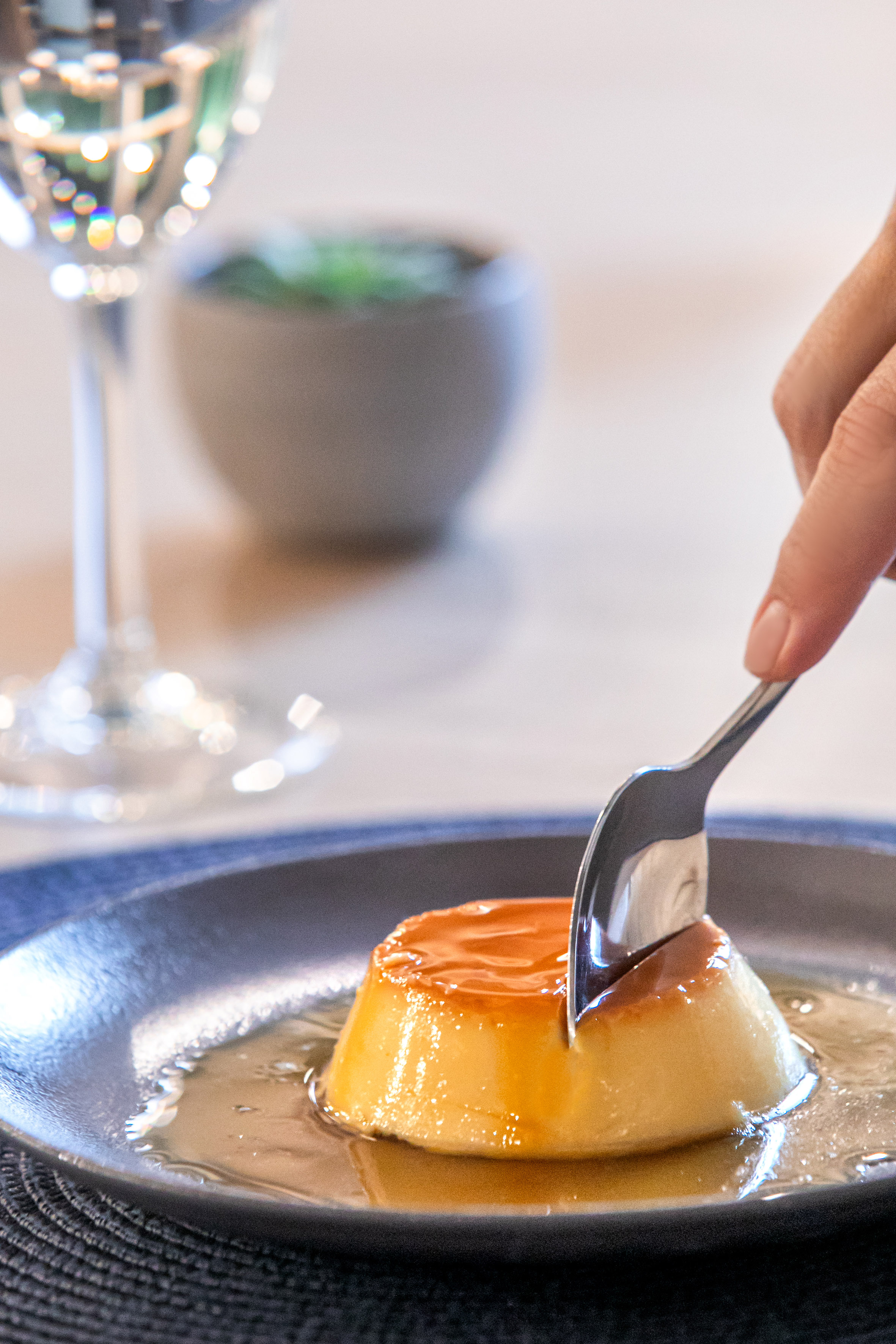 a hand holding a spoon over a flan