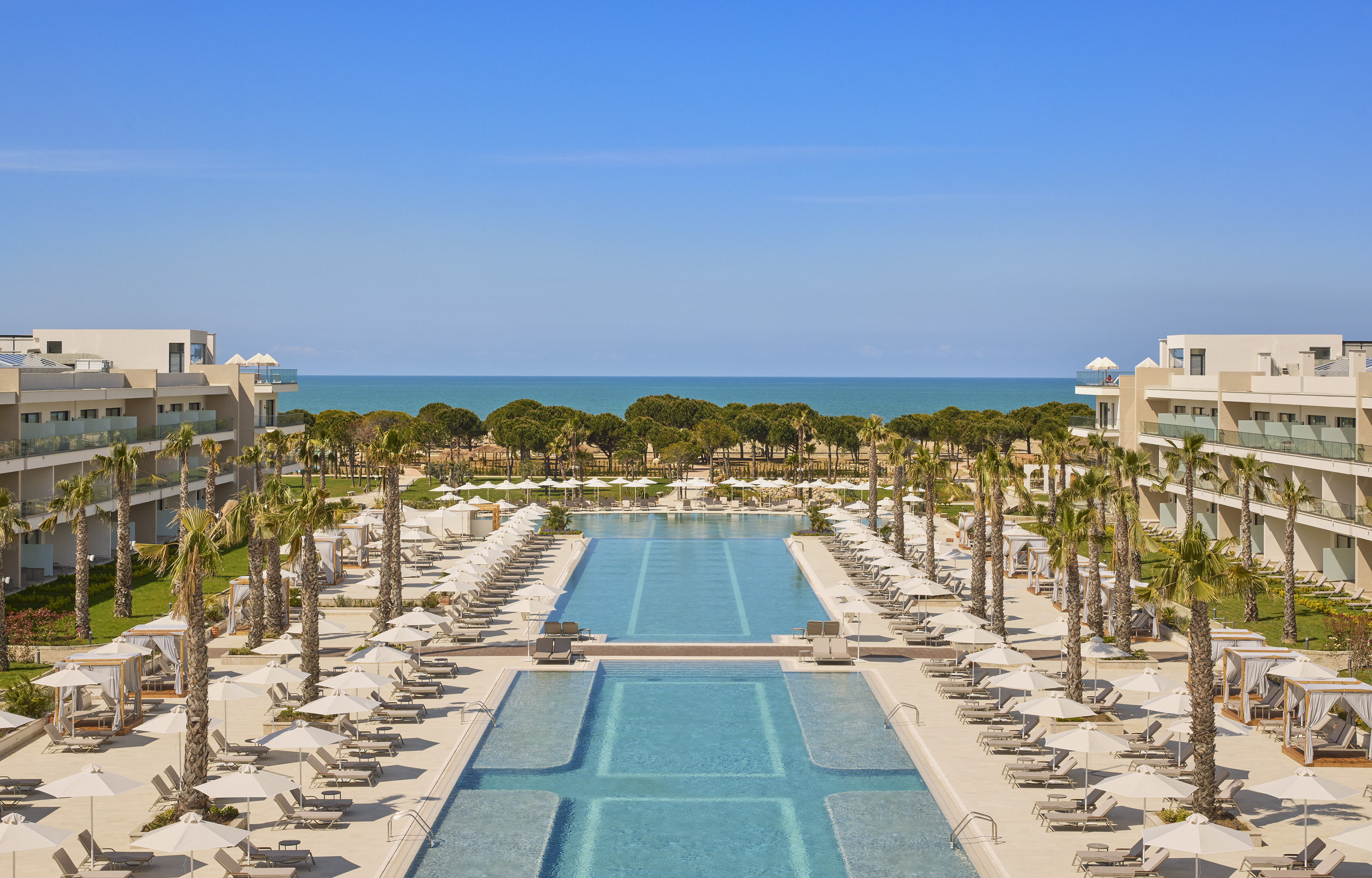 Sunny oceanfront luxury resort with large swimming pools and palm trees.