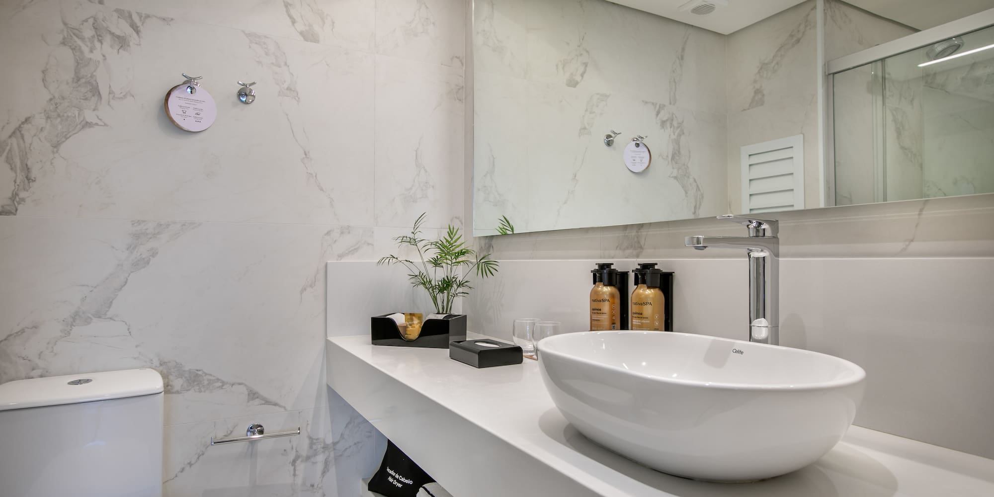 Modern hotel bathroom with white marble walls, vessel sink, and chrome faucet.